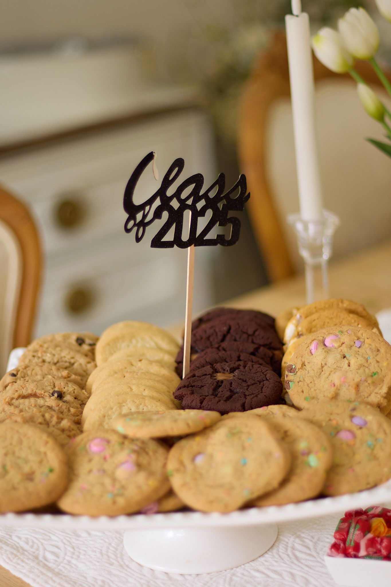 A plate of assorted cookies decorated with a 'Class of 2025' cake topper and a white candle.