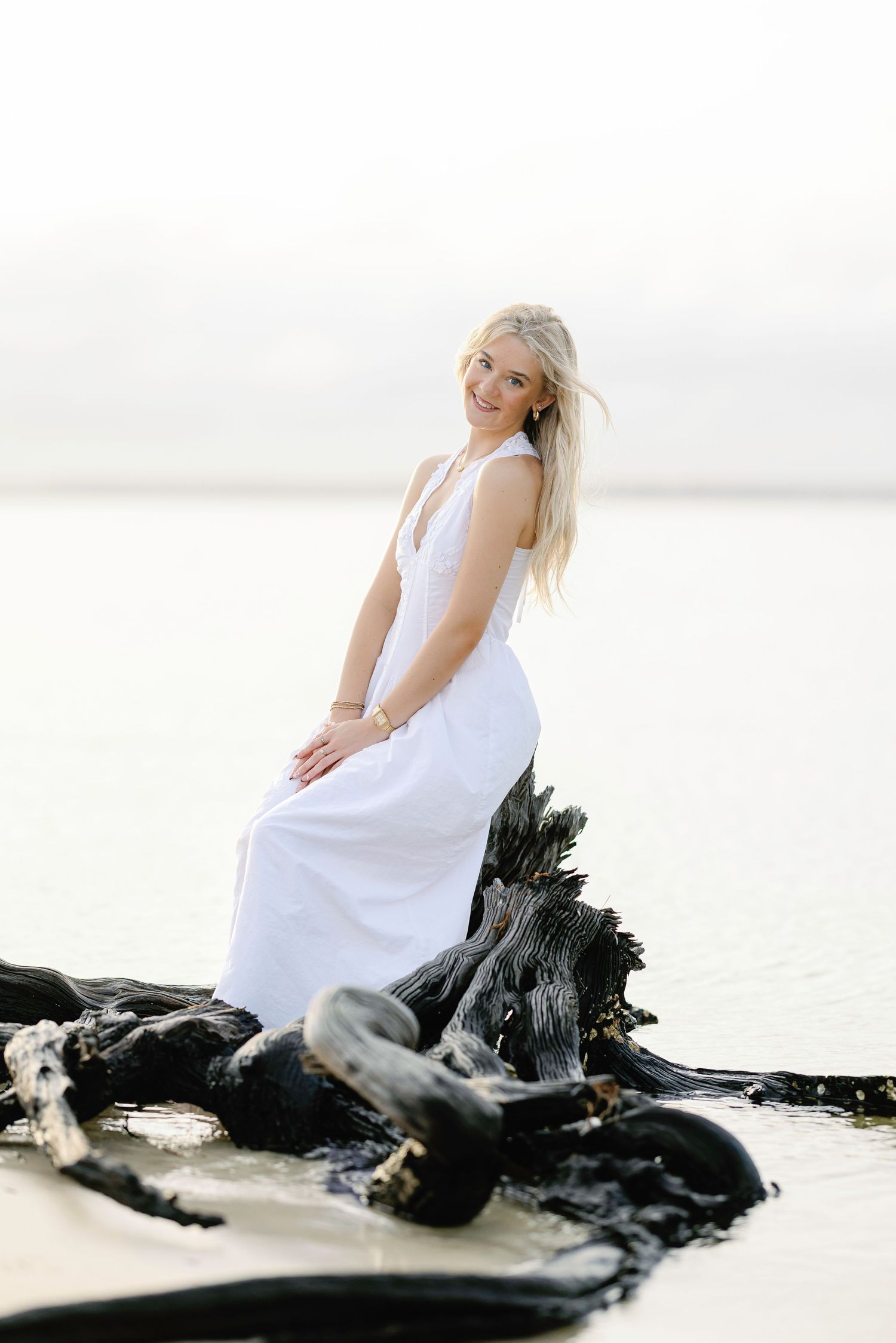 Artistic beach portrait on driftwood featuring white dress against serene water background.
