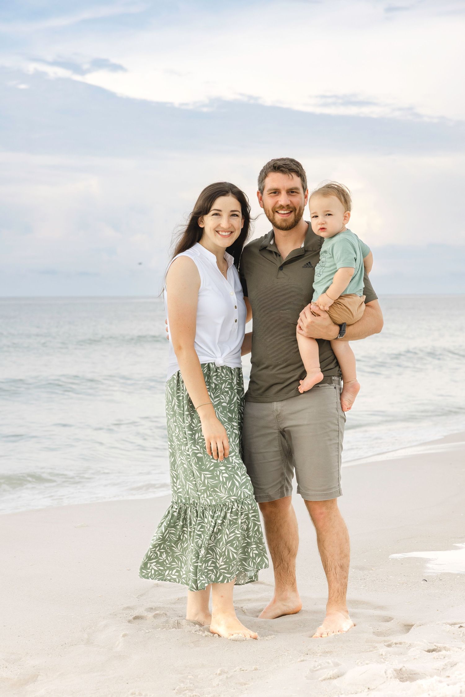 A loving family enjoys a beach photoshoot together on a sandy shore at sunset.