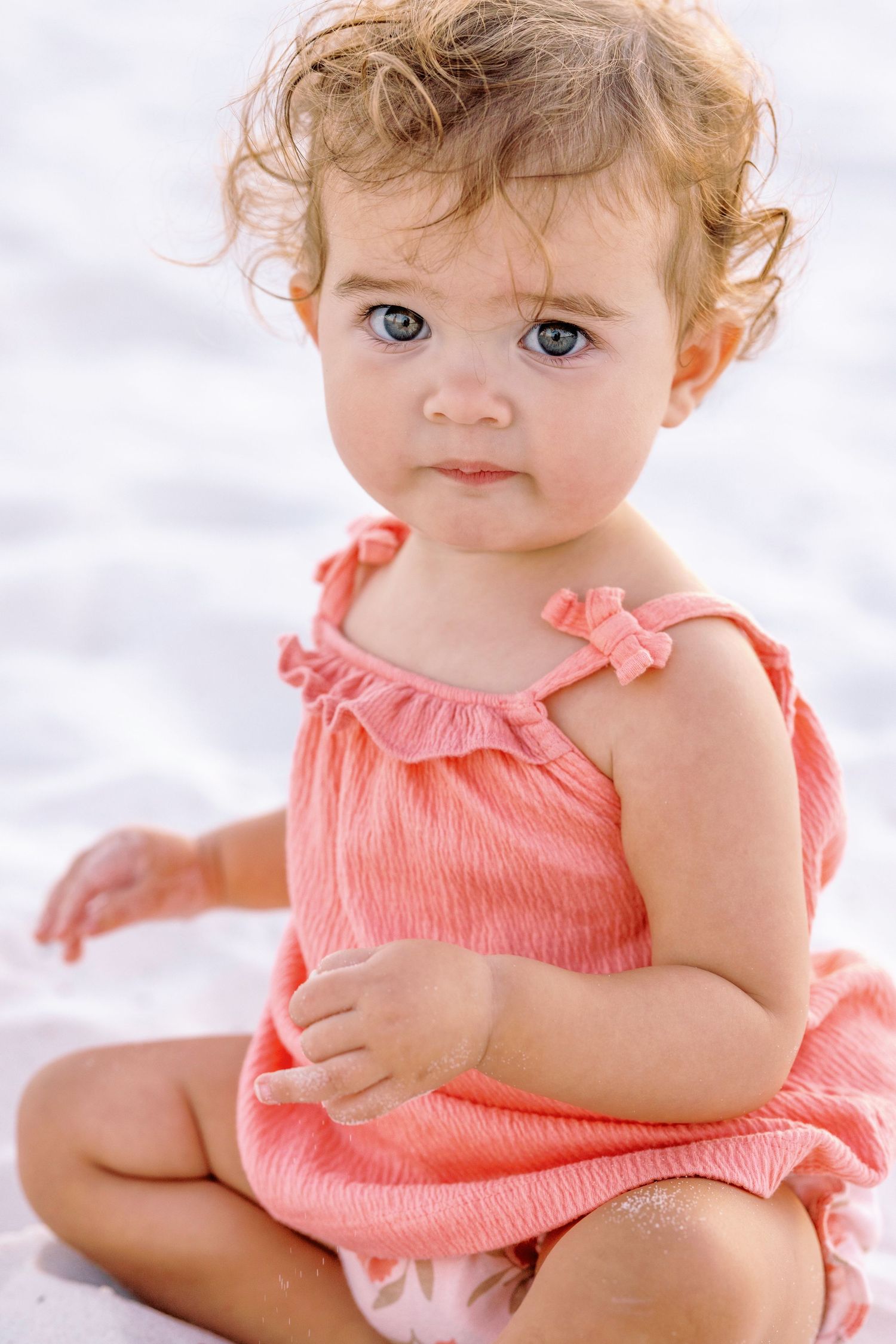 A baby in a coral-colored dress sits on white background in multiple candid poses showing playful expressions.