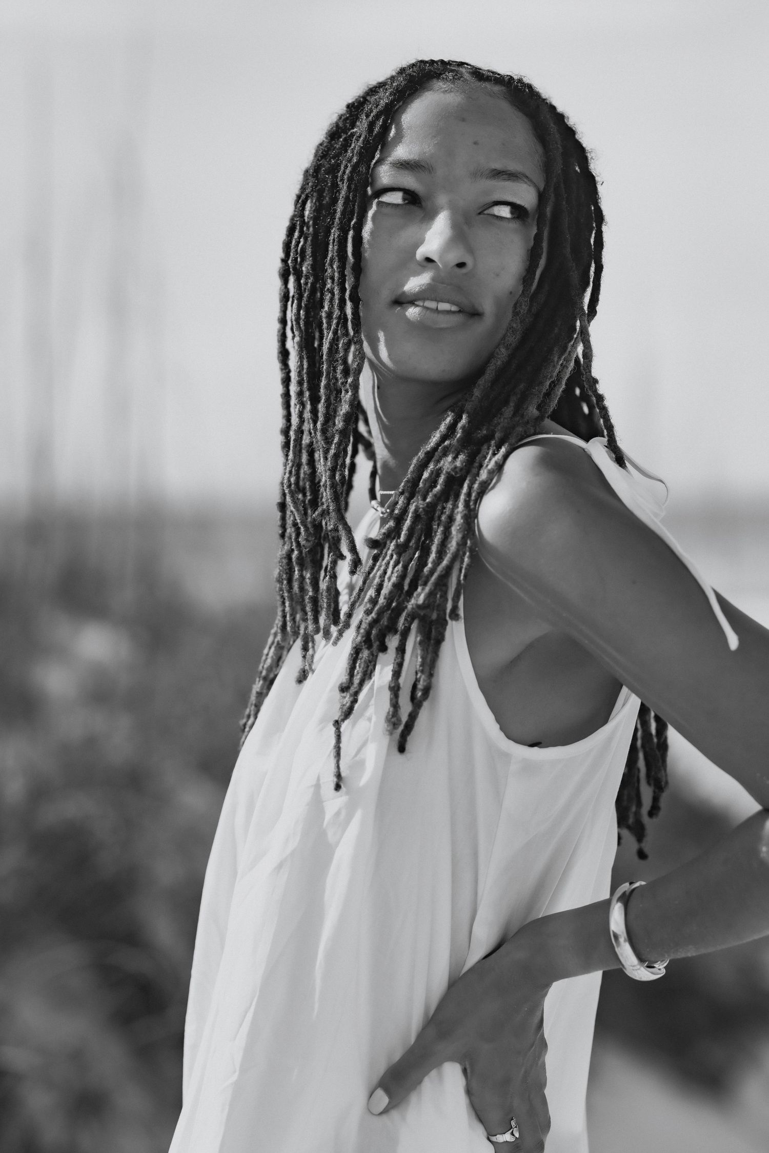 Black and white portrait of a Black woman with long dreadlocks in a white dress outdoors.