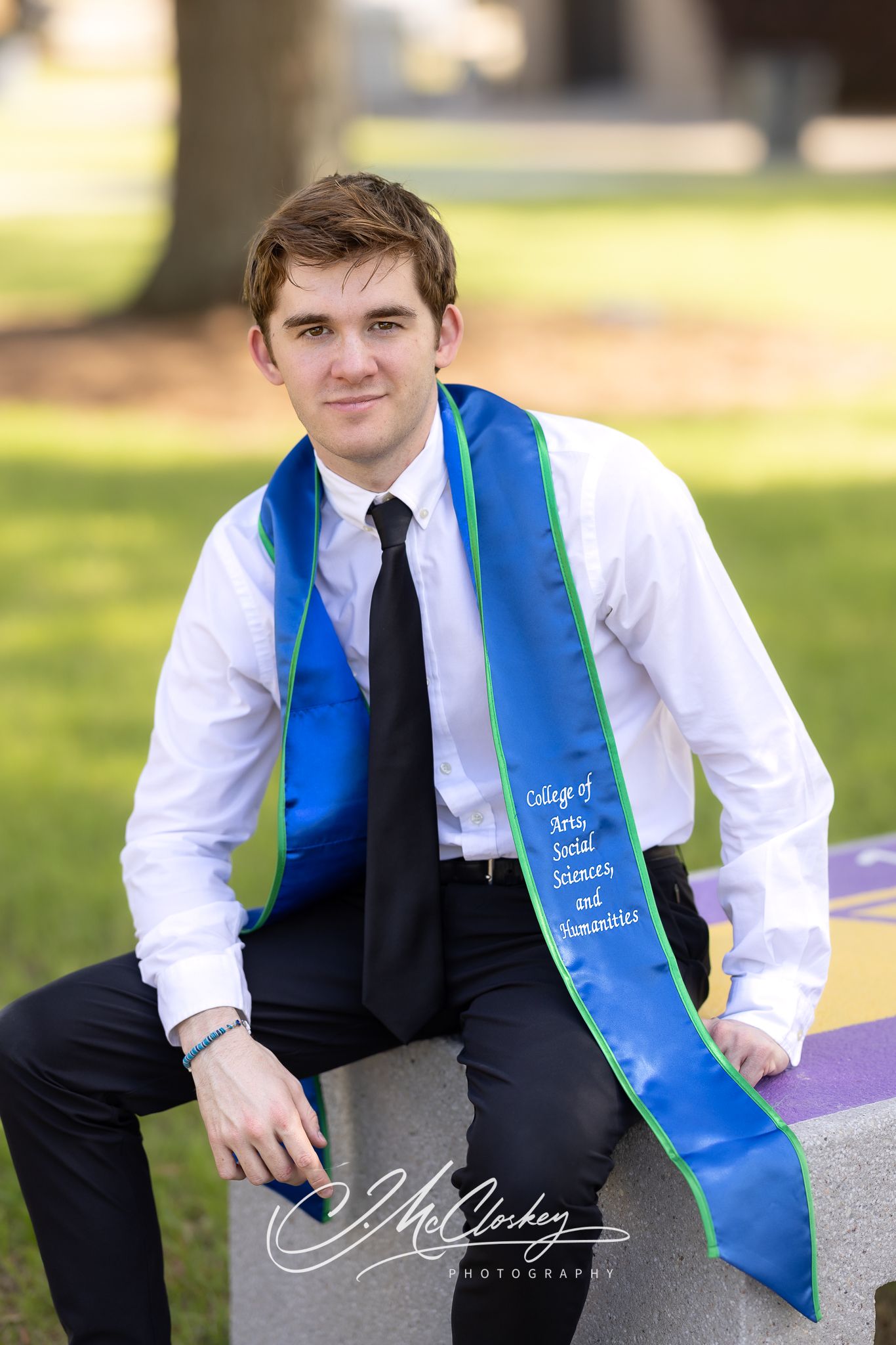 Young male college graduate wearing blue graduation stole from College of Arts, Social Sciences and Humanities.