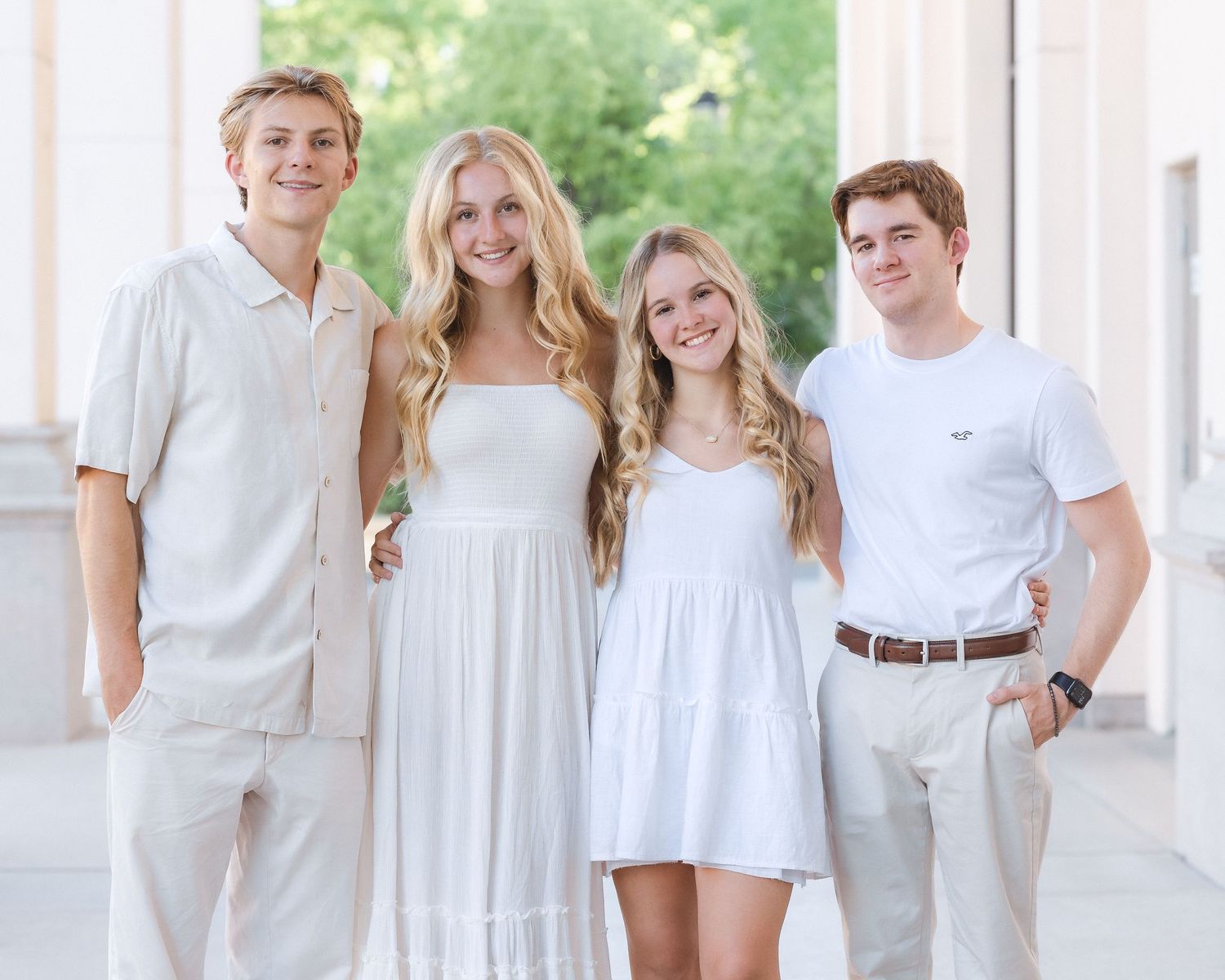 Four young adults smiling together in white and cream outfits for a group portrait.