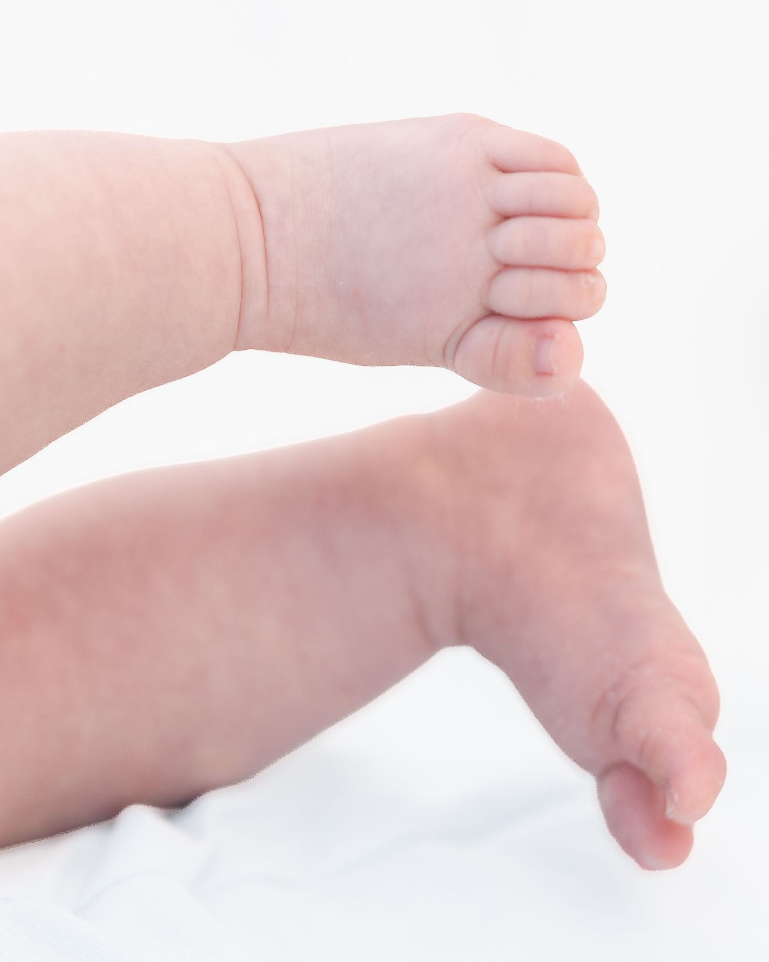 Close-up of a newborn baby's tiny feet and hand resting on a white soft surface.