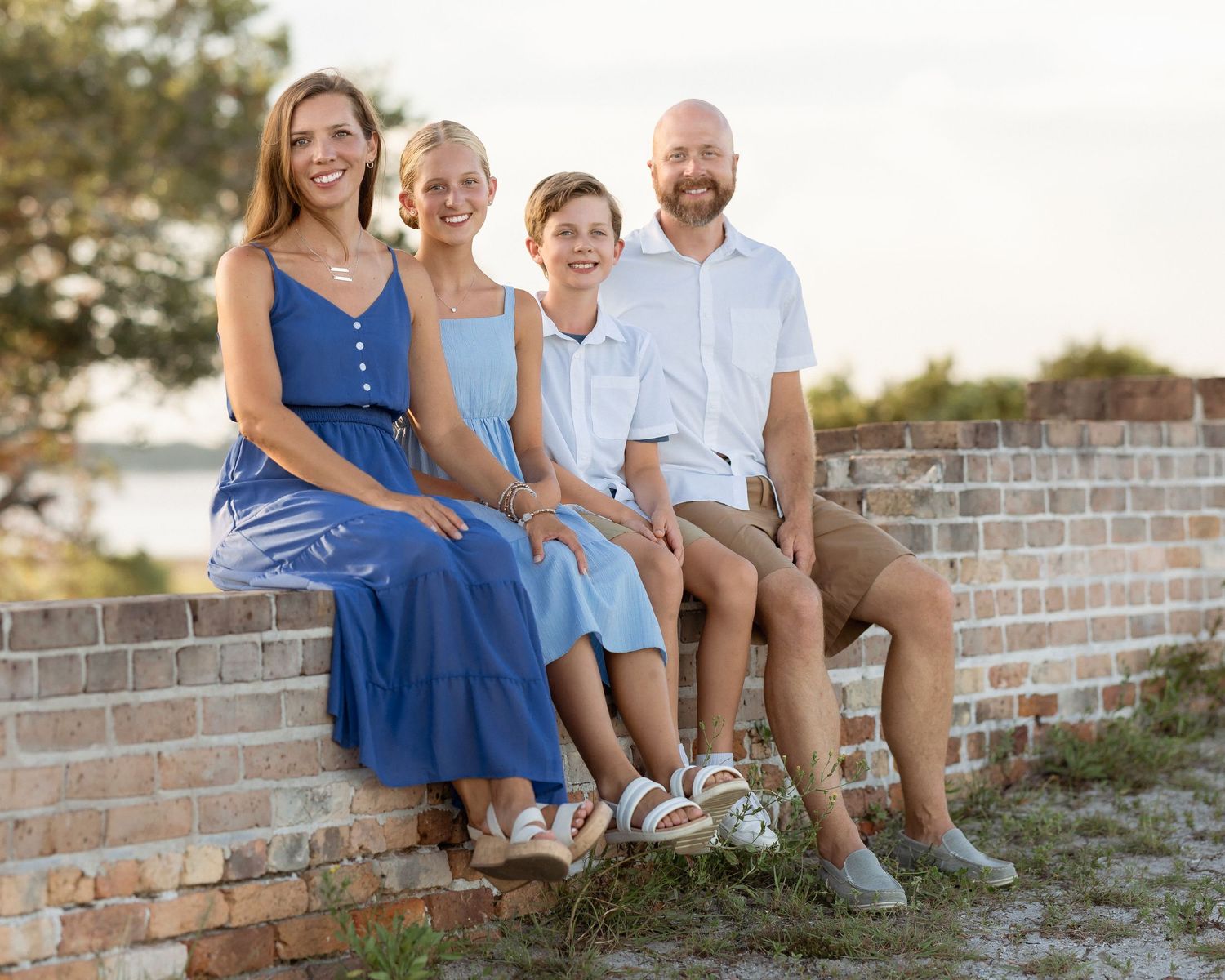 Happy family of four sitting on a brick wall outdoors, smiling in coordinated blue and white outfits.