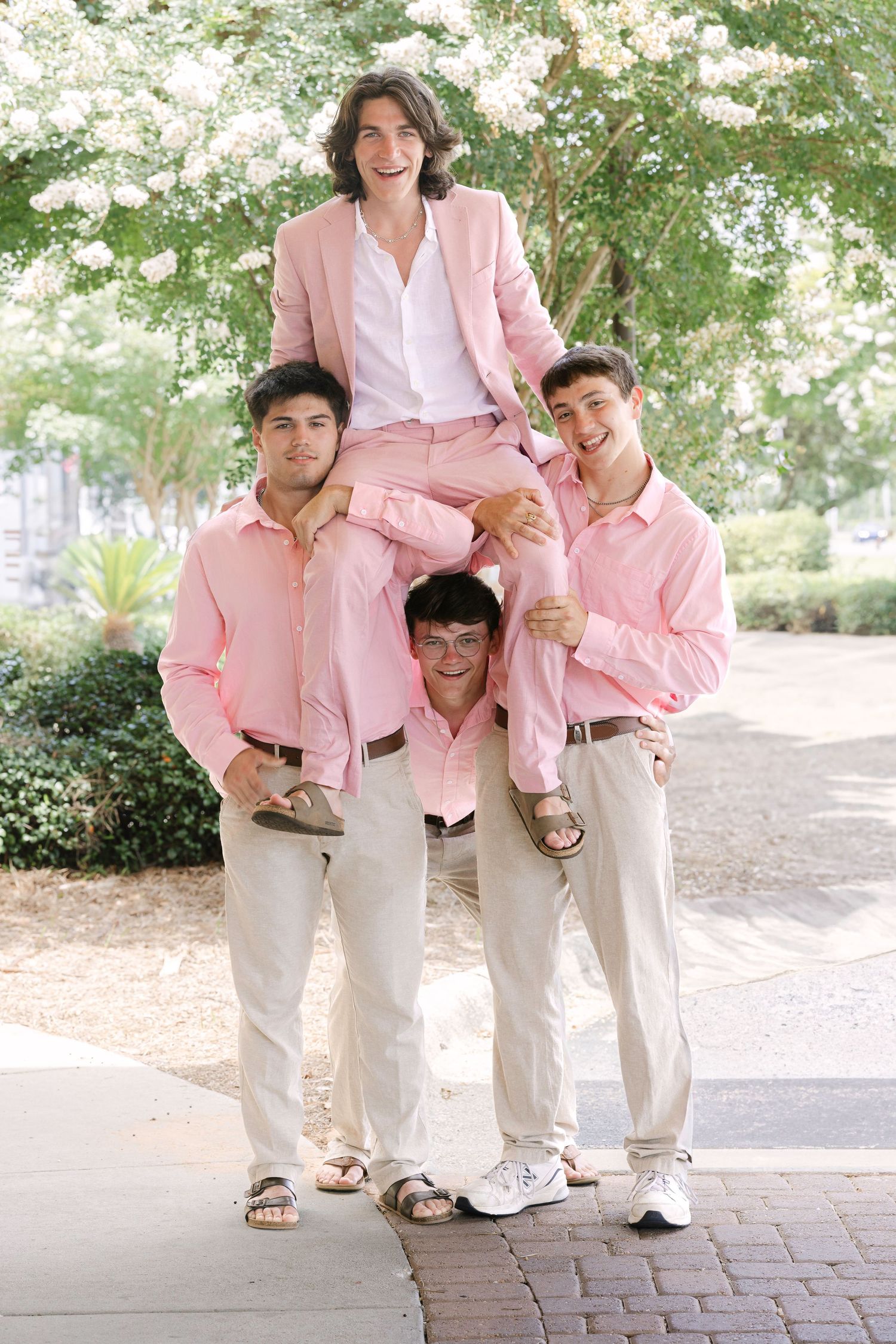 A group in matching pink blazers and light colored pants pose playfully on a brick pathway.