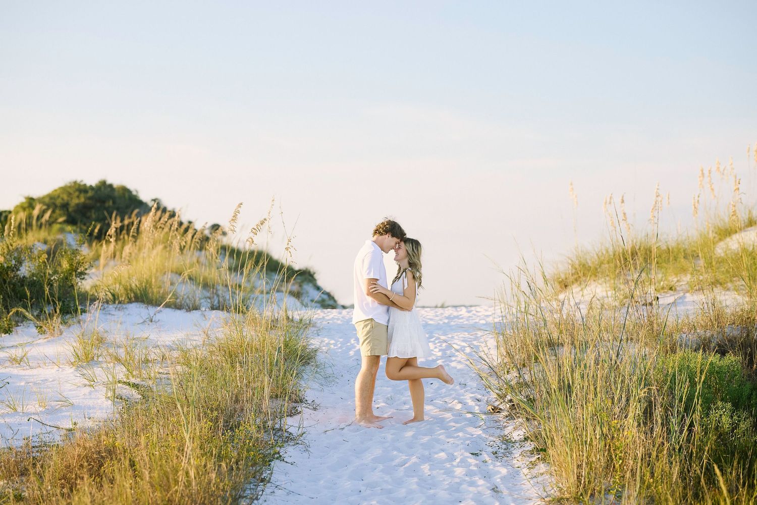 A tranquil sunset scene over sand dunes with sea oats swaying in the warm golden light along a beach shoreline.