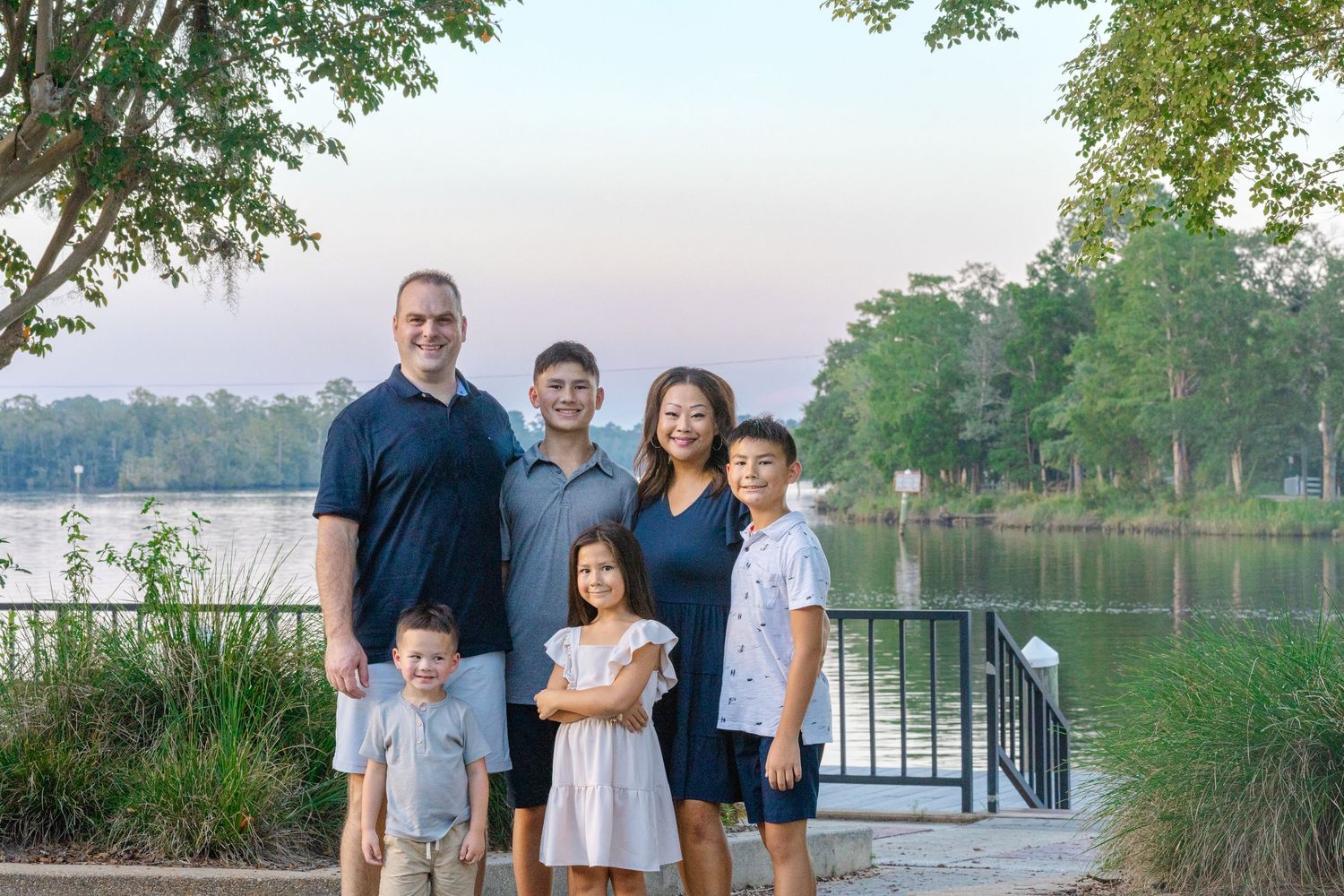 Group posing for a photo by a scenic lake with trees and water in the background.