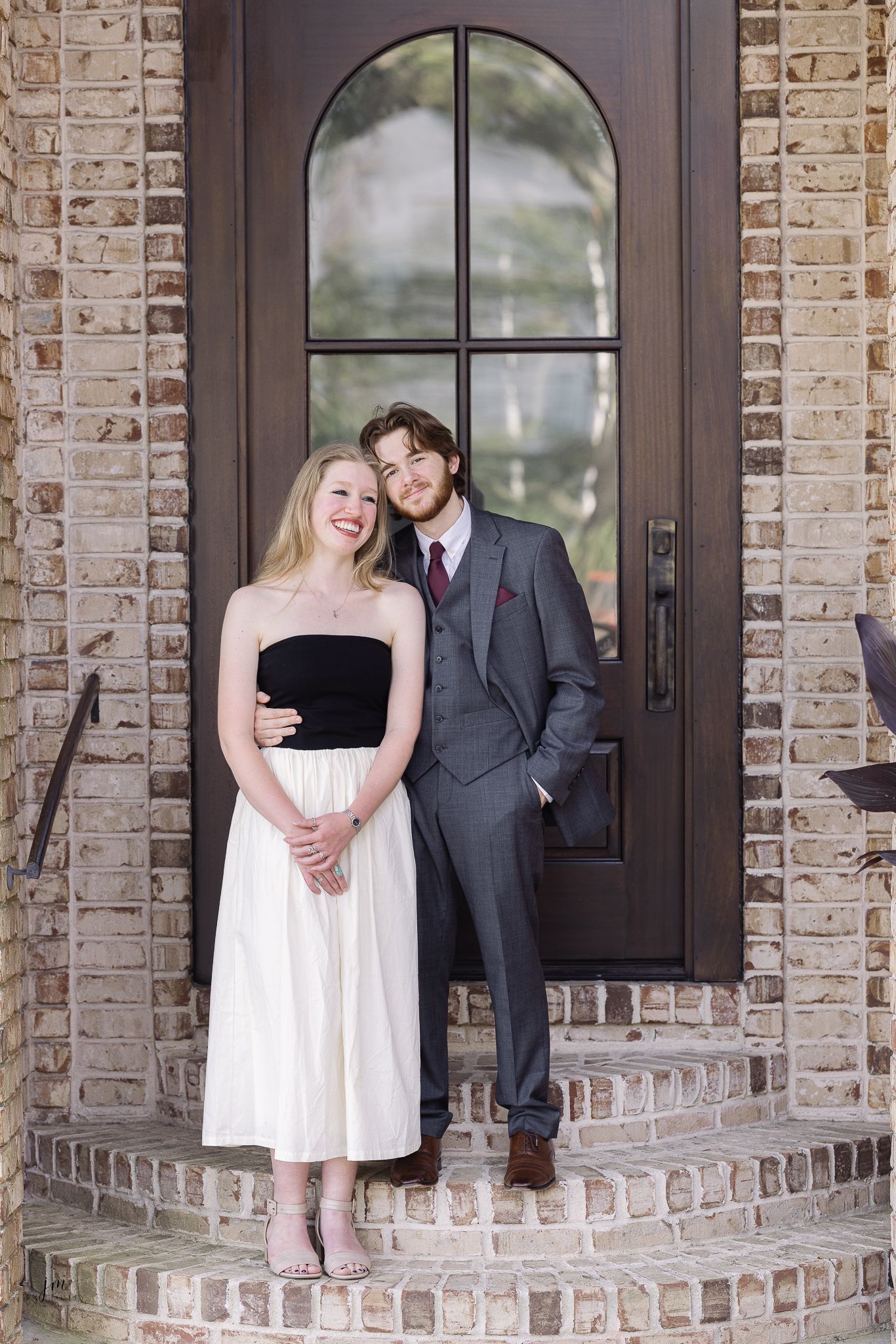 A couple shares an intimate moment on brick steps in front of a dark wooden door.