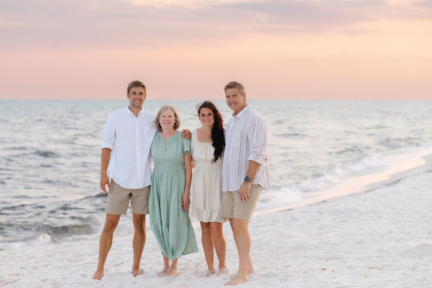 A small group stands together on a white sandy beach at sunset with ocean waves in the background.