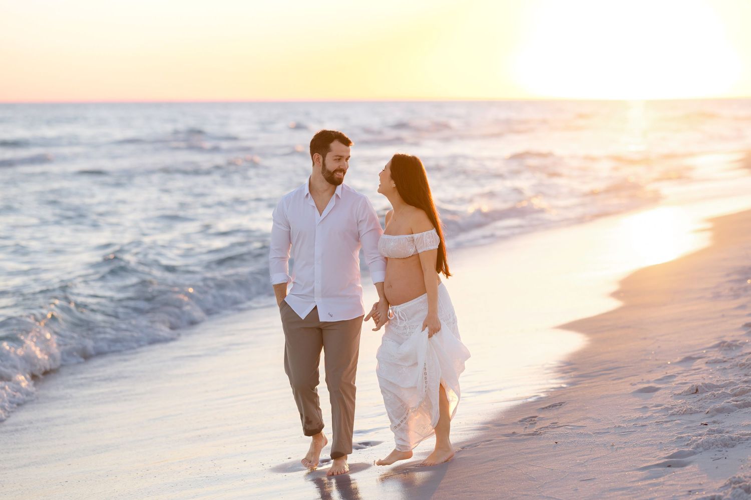 Couple walking together on a sandy beach at sunset with waves rolling in along the shoreline.