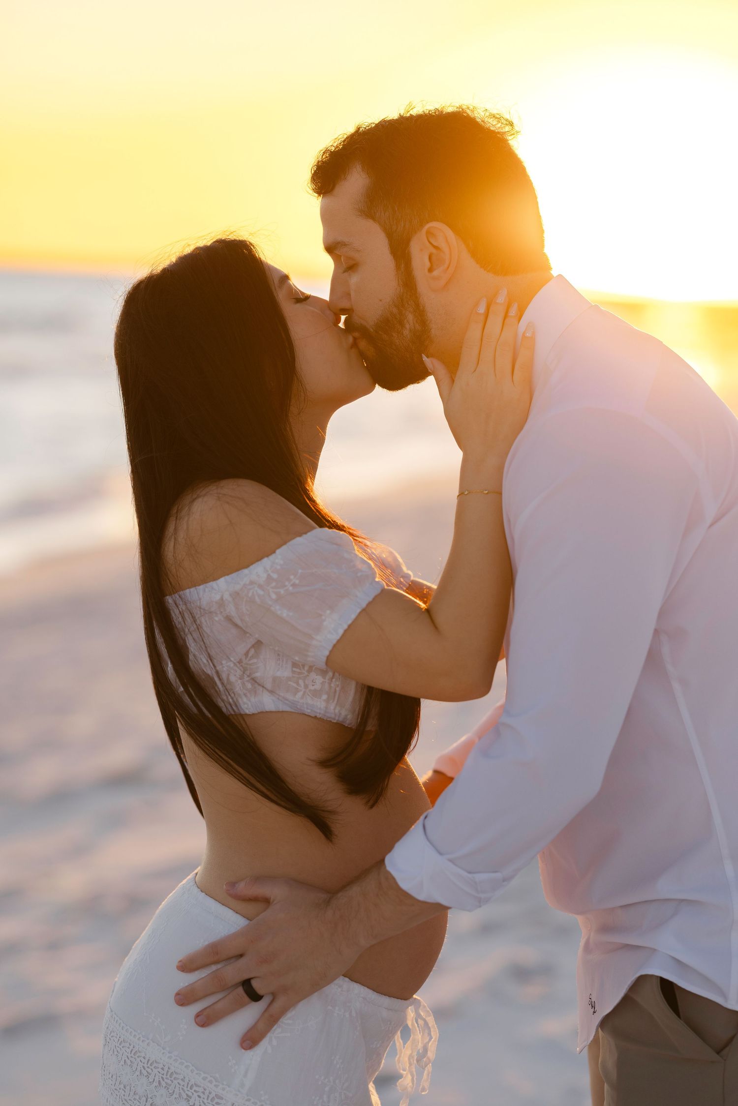 Romantic couple embraces on beach at golden sunset creating silhouette against warm glowing sky.