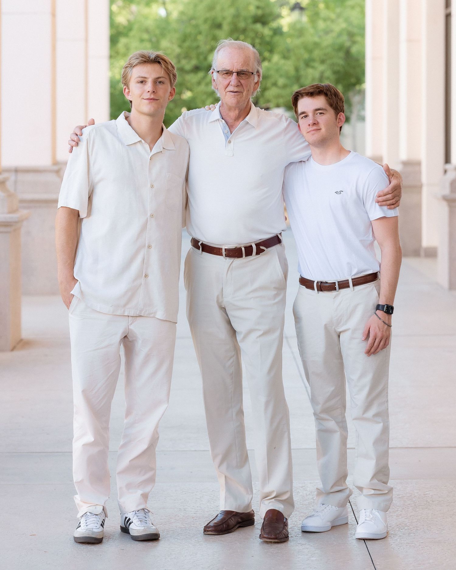 Three males in white and beige outfits posing together between columns.