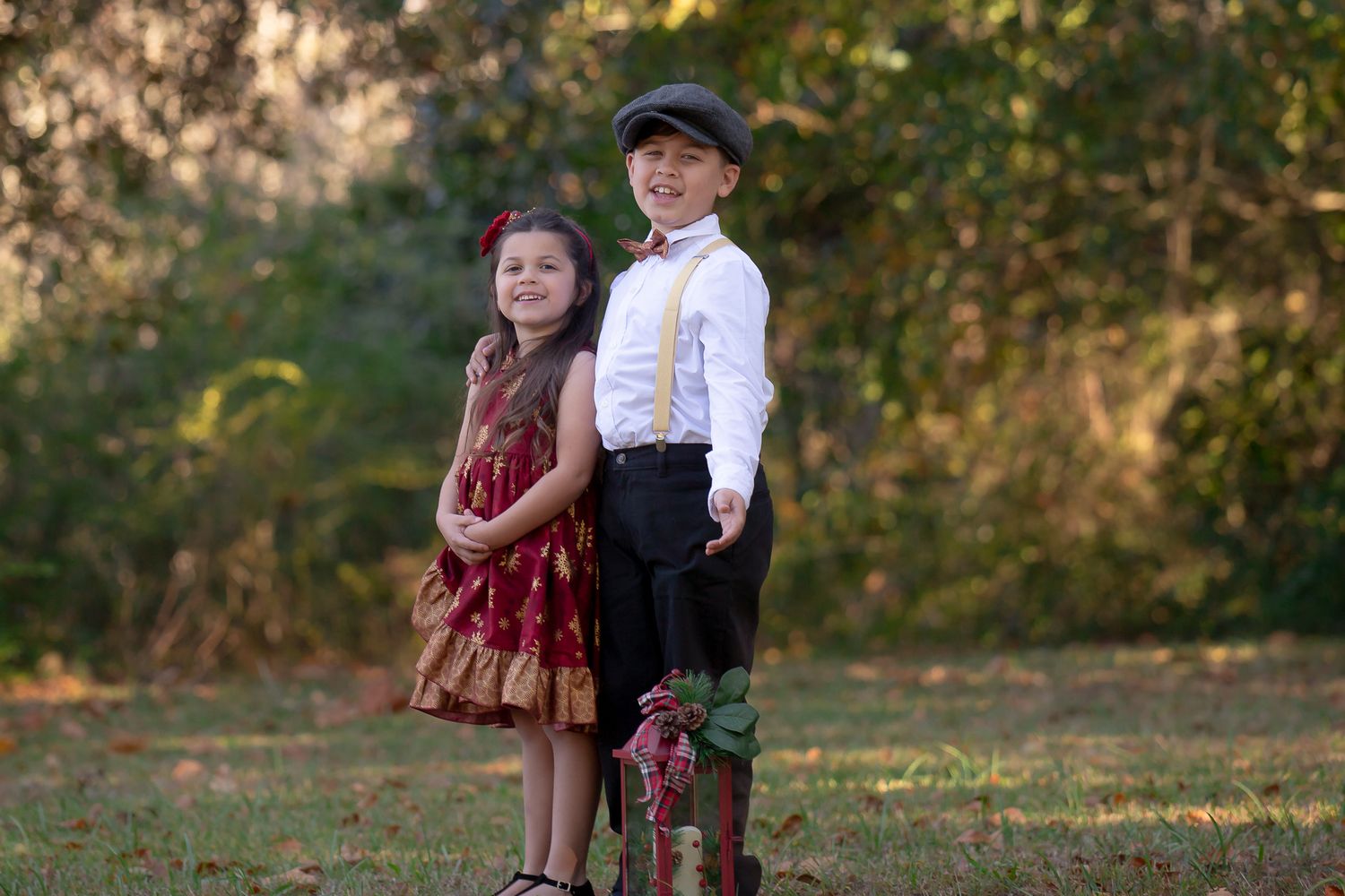 Two young children in vintage style clothing sitting together in an autumn outdoor setting.