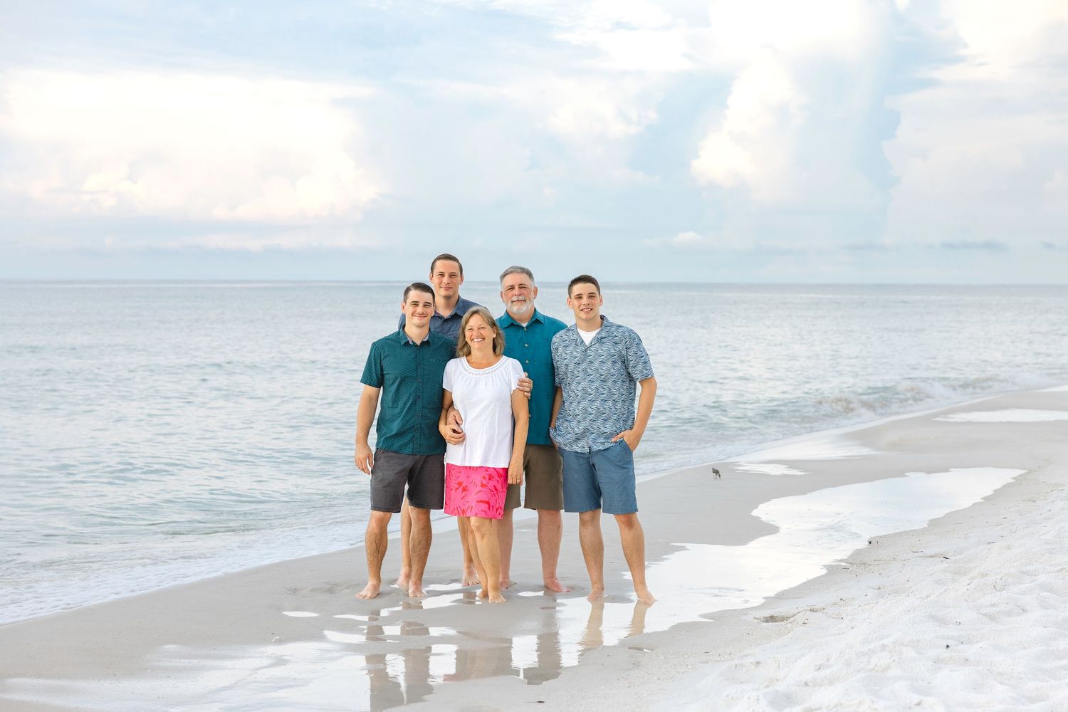 A group of people stand together smiling by the ocean shoreline during a beachfront photo session.
