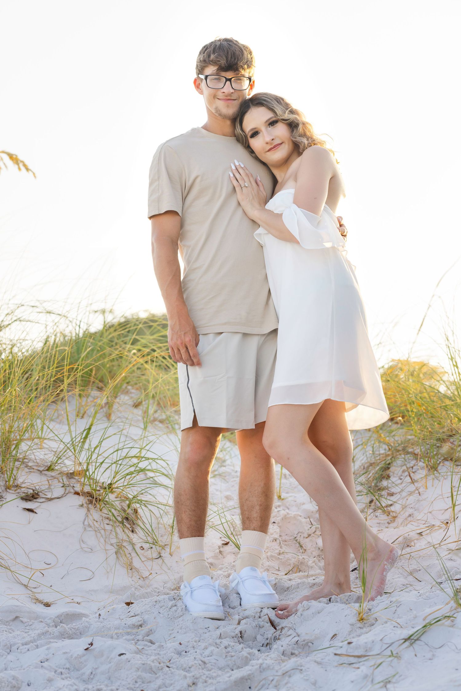 Two people walk together along white sandy dunes with beach grass swaying in the breeze.