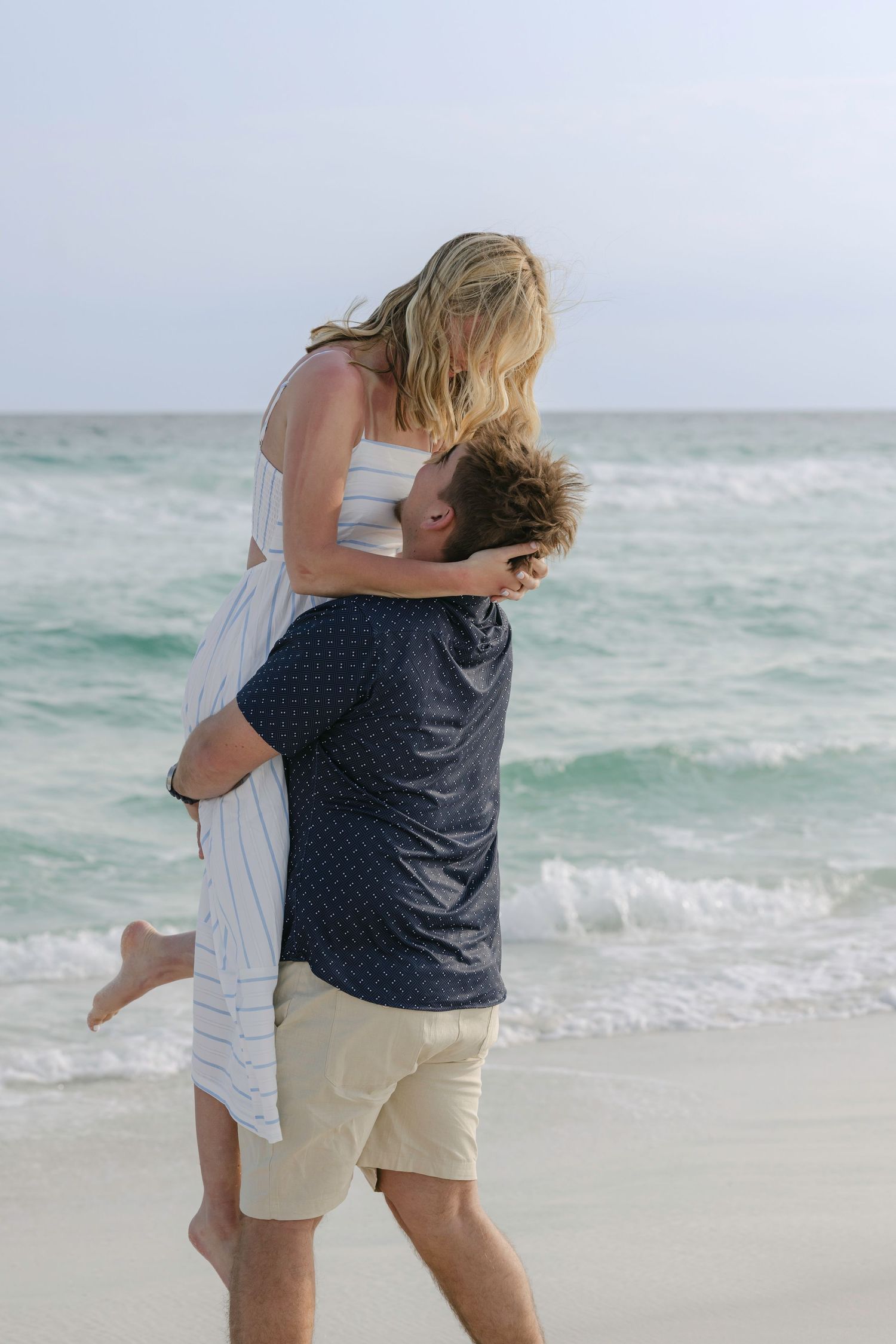 Couple embracing romantically on a sandy beach with turquoise ocean waves in the background.