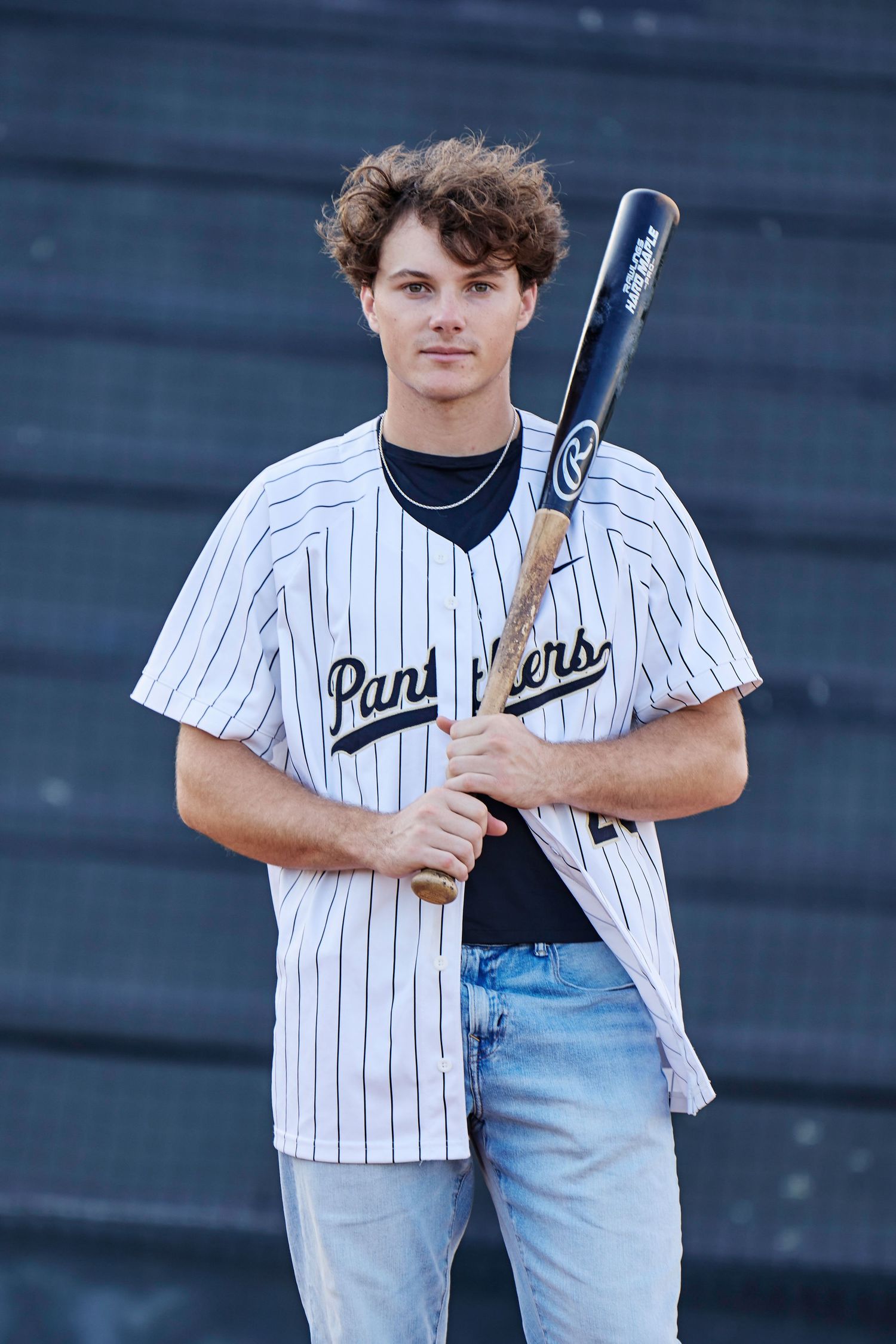 Young male baseball player in Panthers pinstripe jersey holding a bat, posing outdoors for a portrait photo.