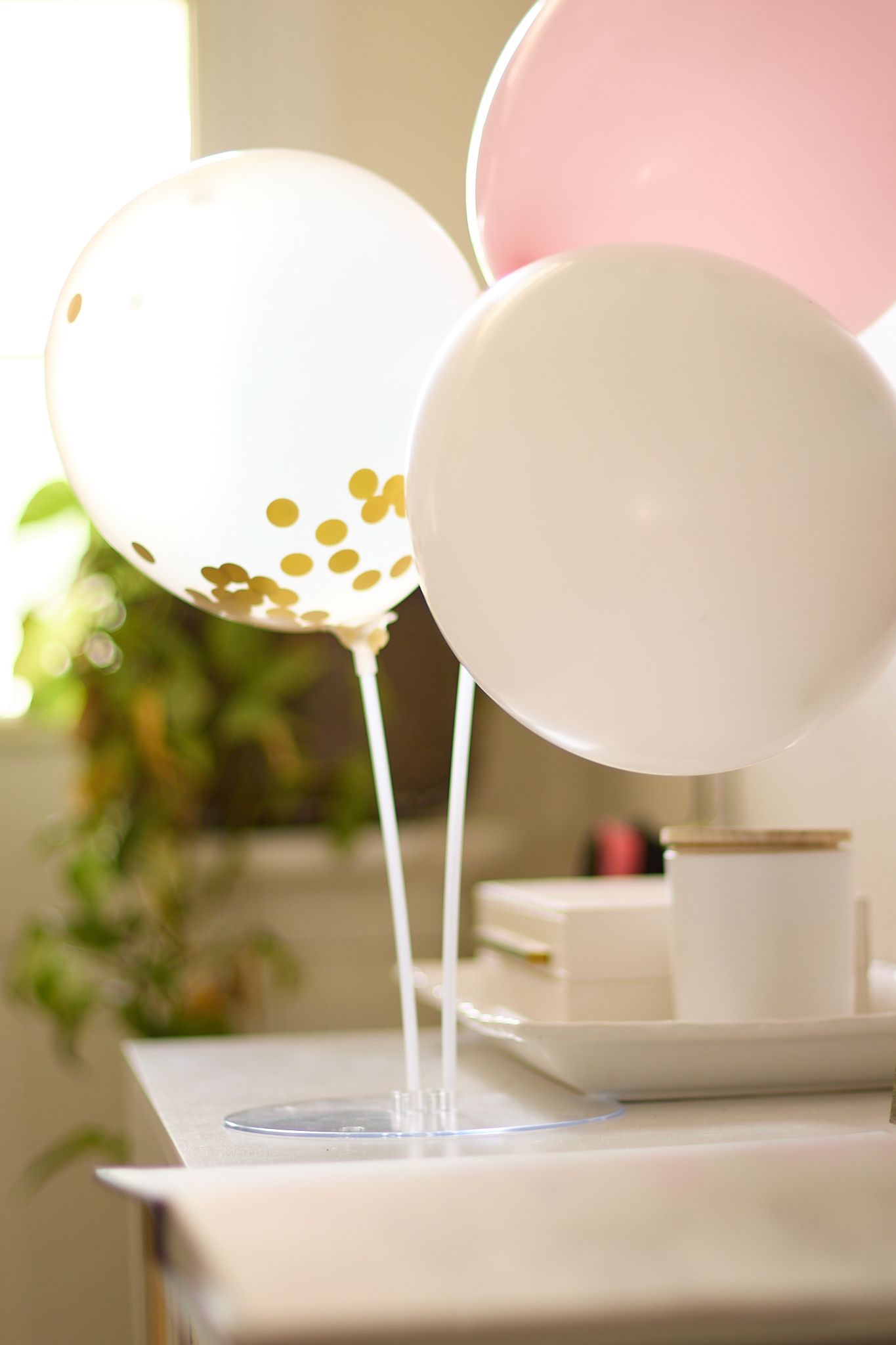 Elegant white and pink balloons with gold confetti decorating an indoor celebration.