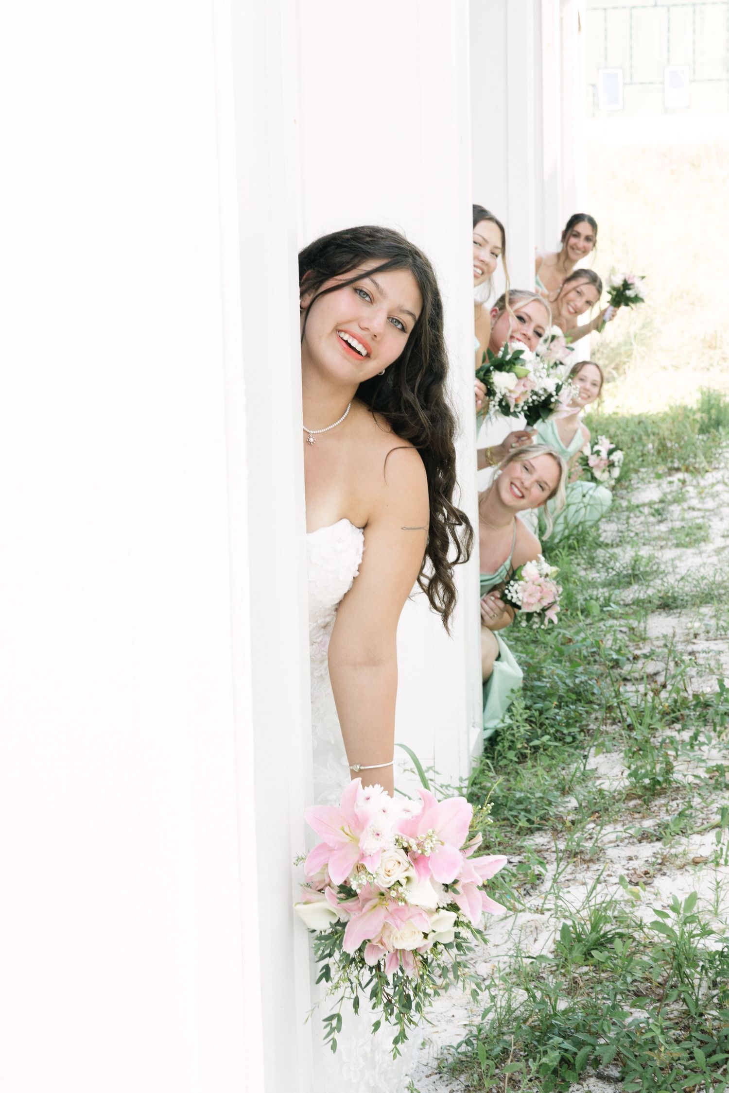Fun wedding party photo with people peeking playfully from behind a white column.