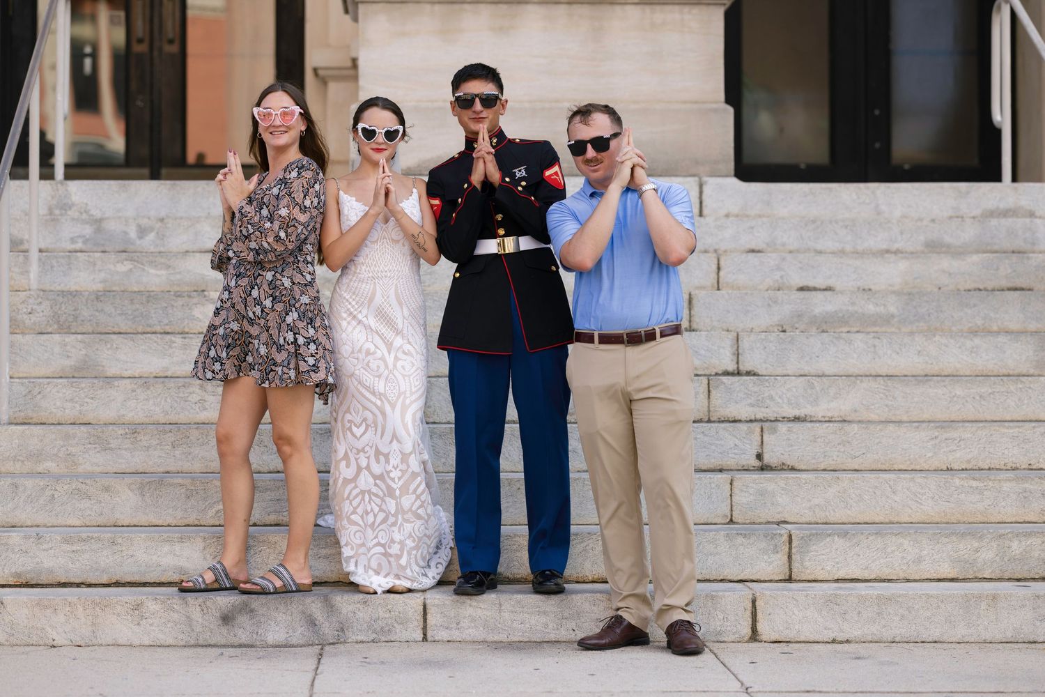 Marine in dress uniform poses with family on steps, all making prayer hands gesture.