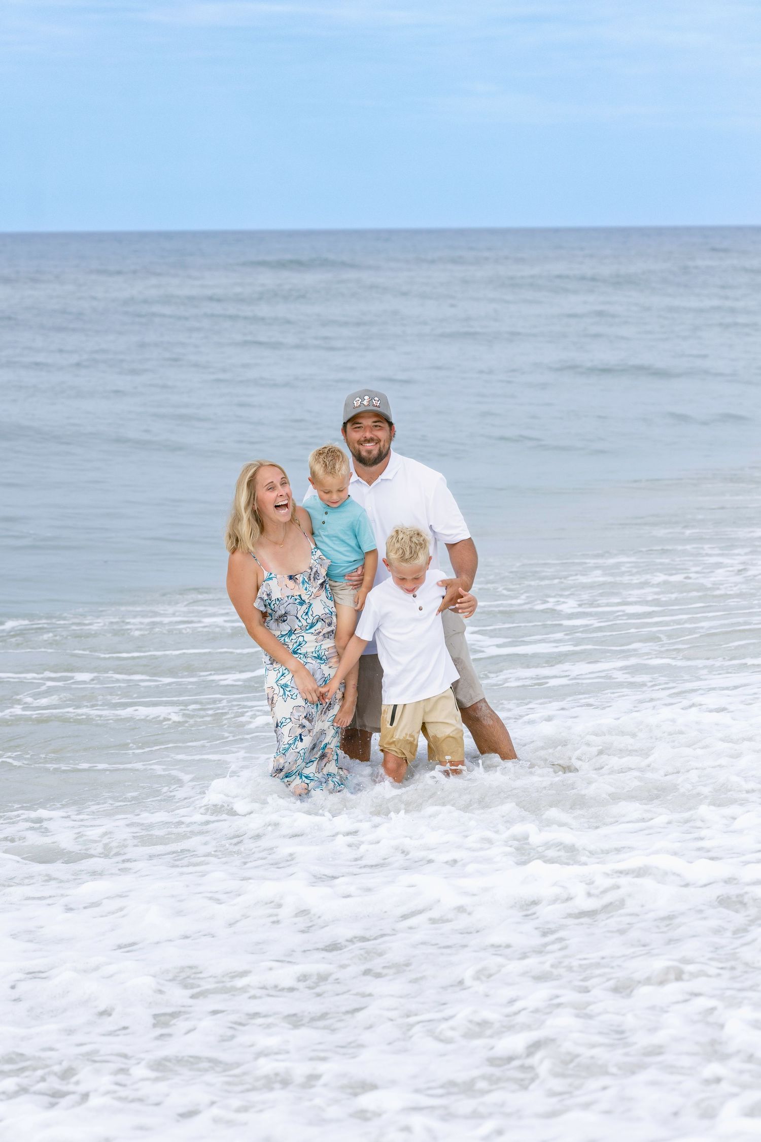 Joyful family of four laughing in ocean waves, parents holding children as water splashes around them.