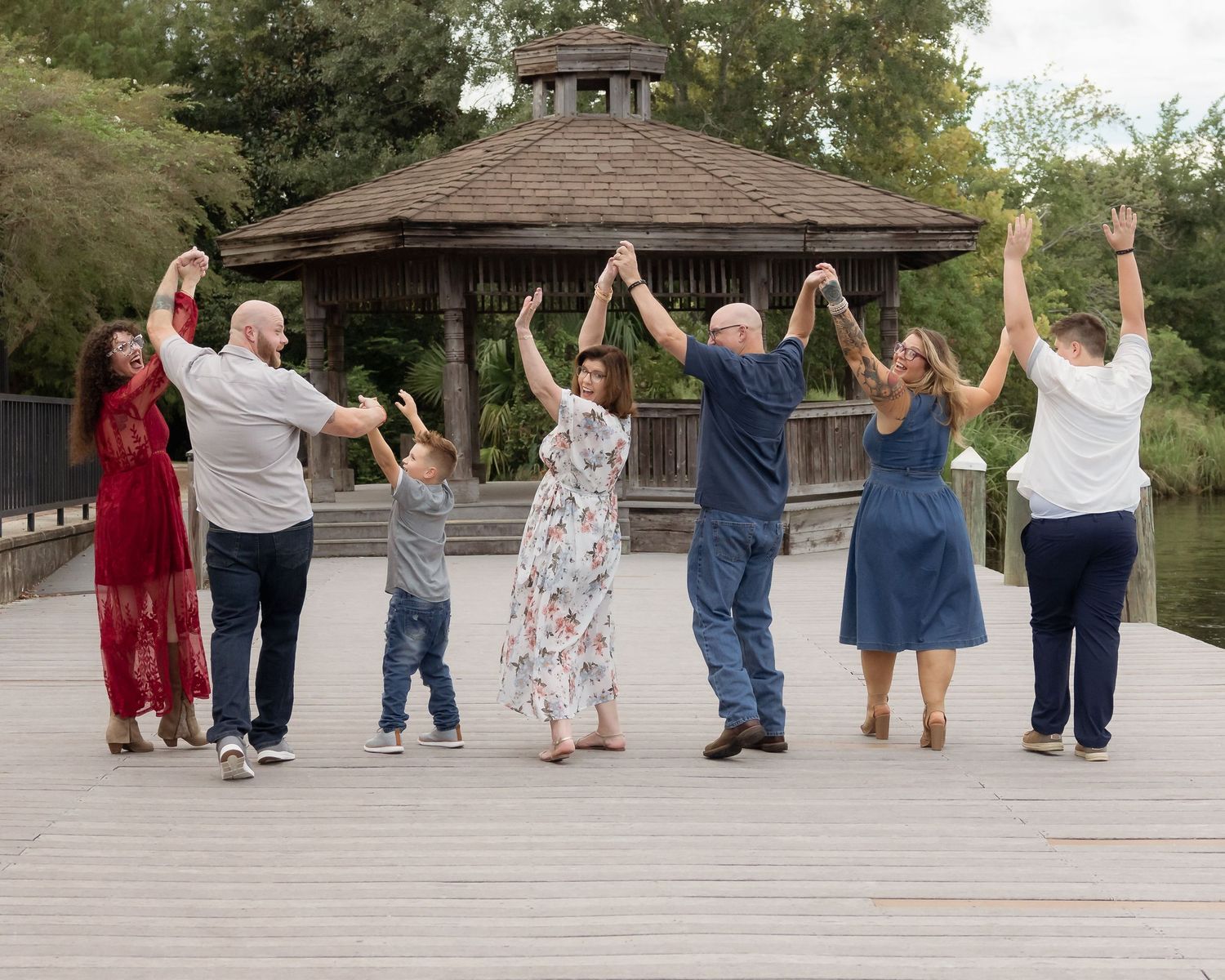 Multi-generational family holding hands in a line on a wooden deck near a gazebo outdoors.