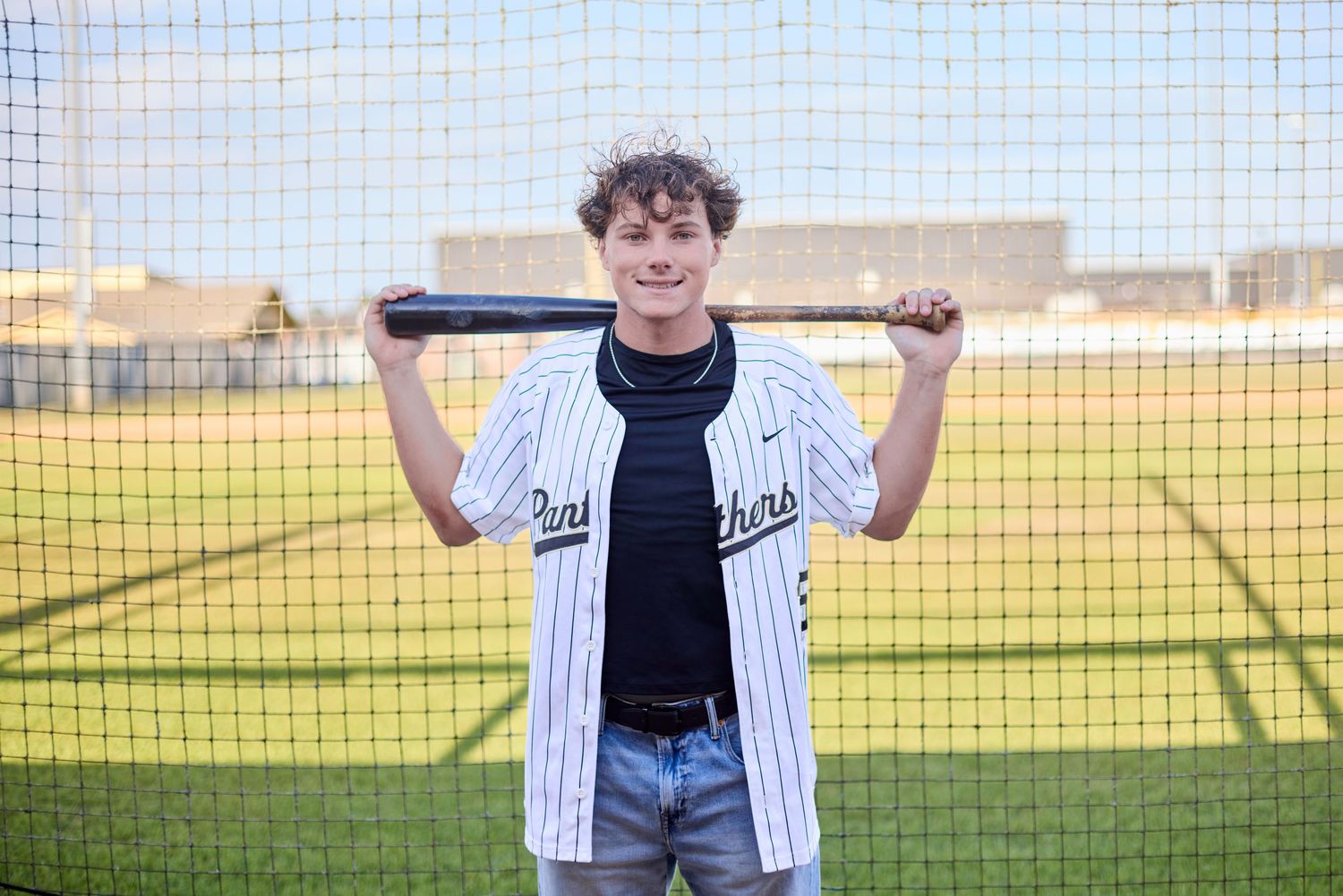 Baseball player posing with bat near batting cage in white uniform.