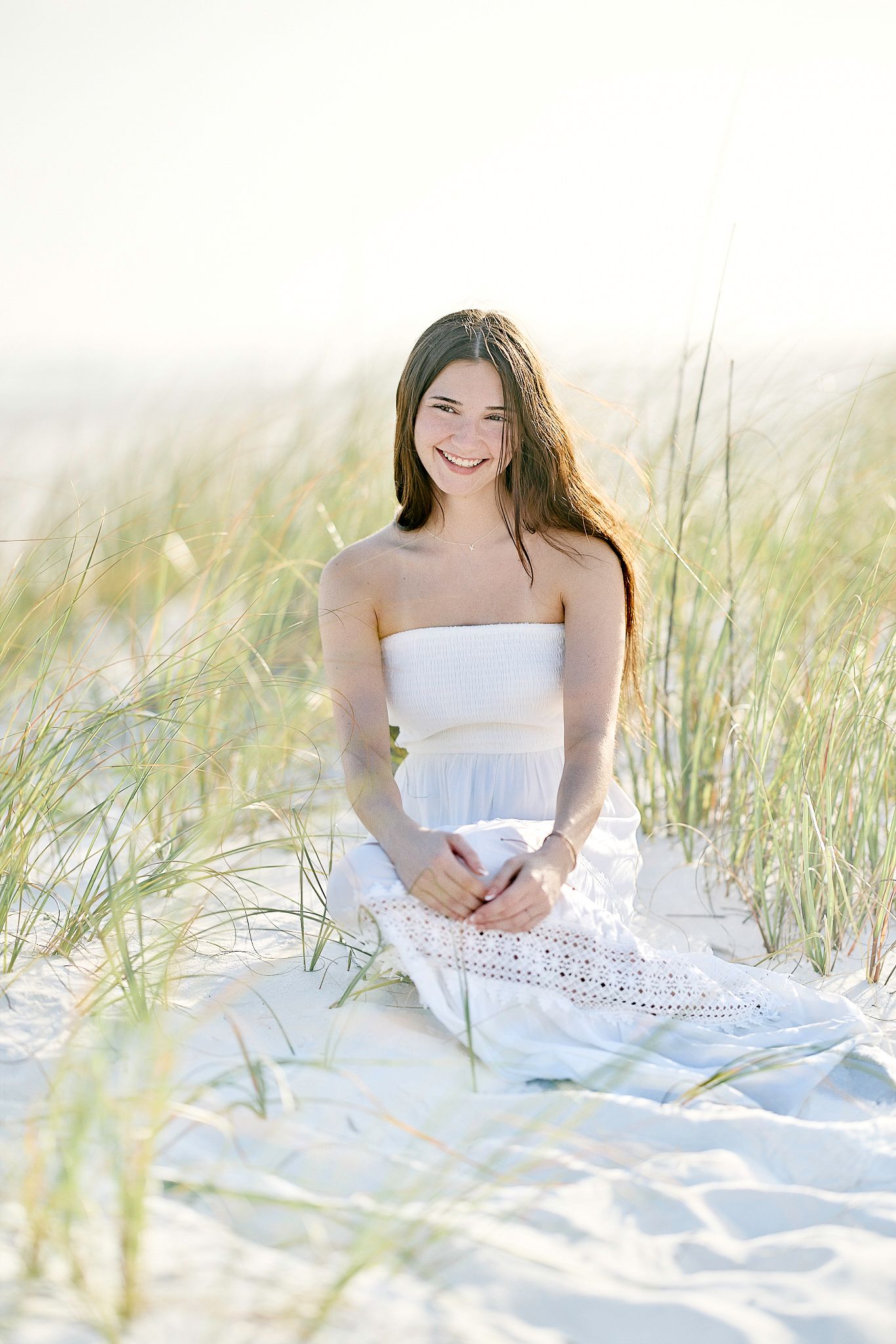 Bright coastal portrait with white dress amid beach grass and sand.