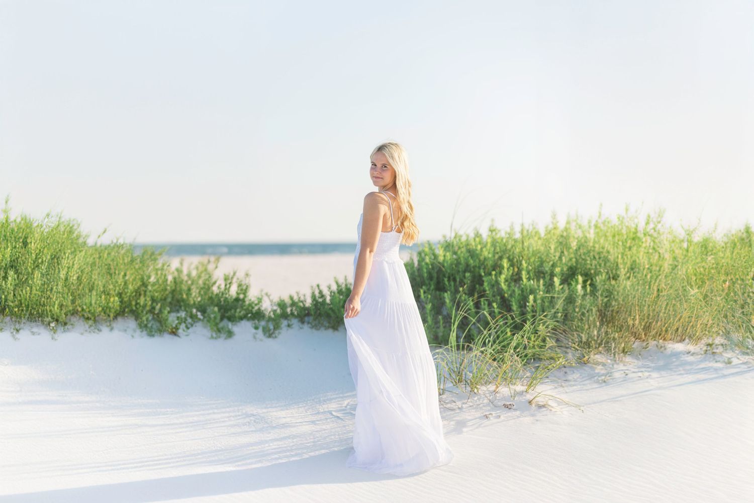 Artistic beach photography with white dress against sand dunes and sea grass.