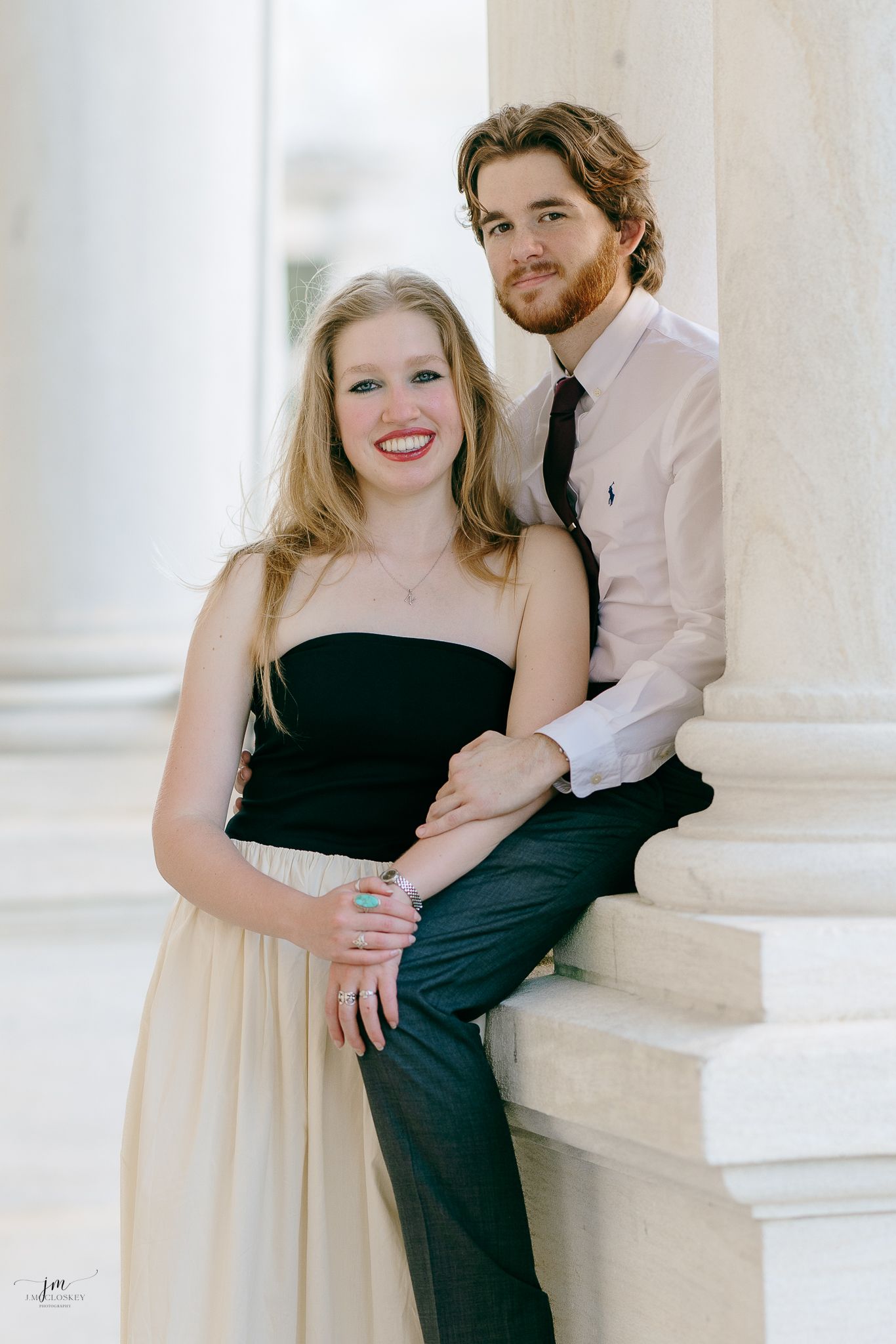 A couple sits together on white marble steps in elegant black and white attire.