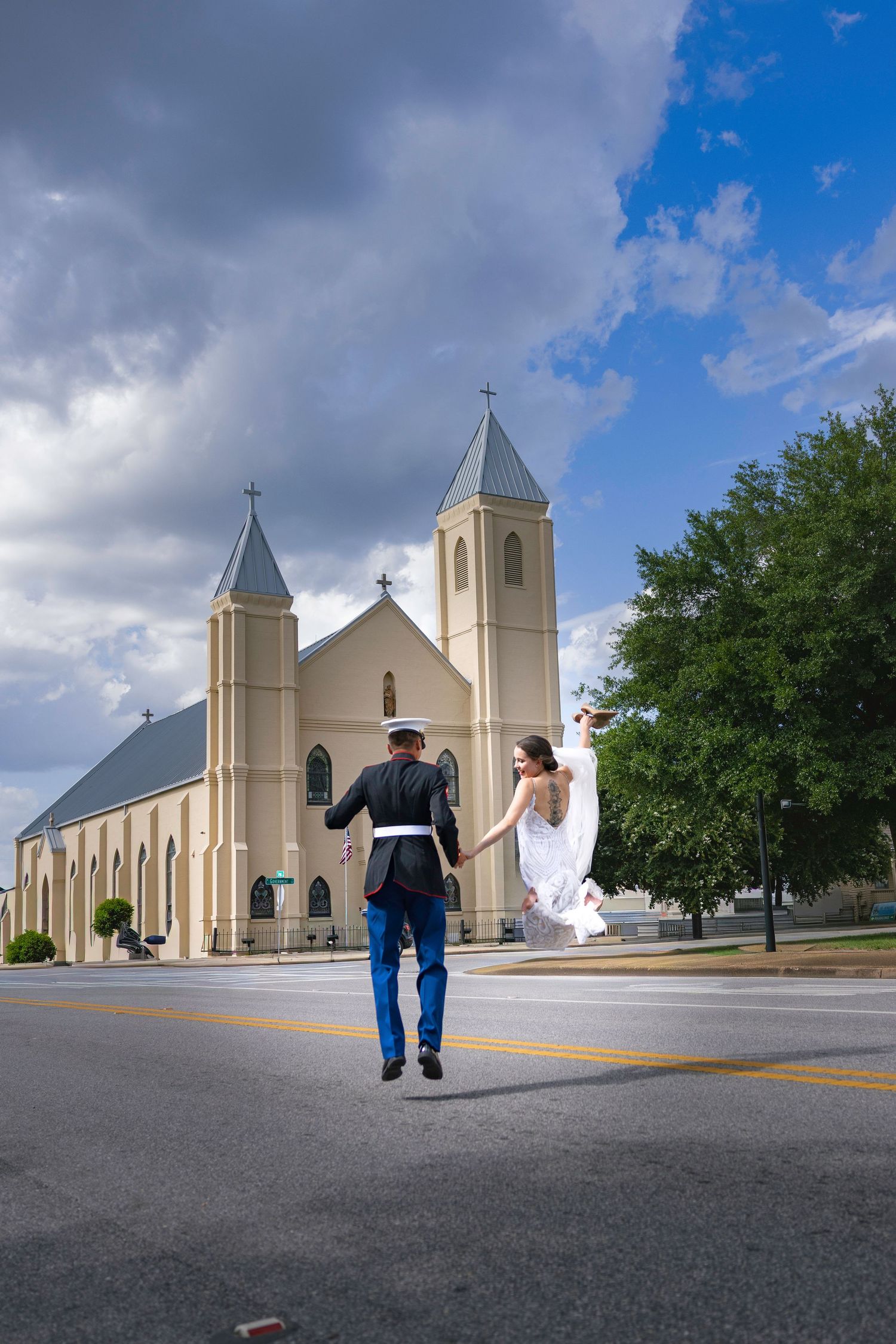 A joyful newlywed couple jumps hand-in-hand in front of a beautiful church on their wedding day.