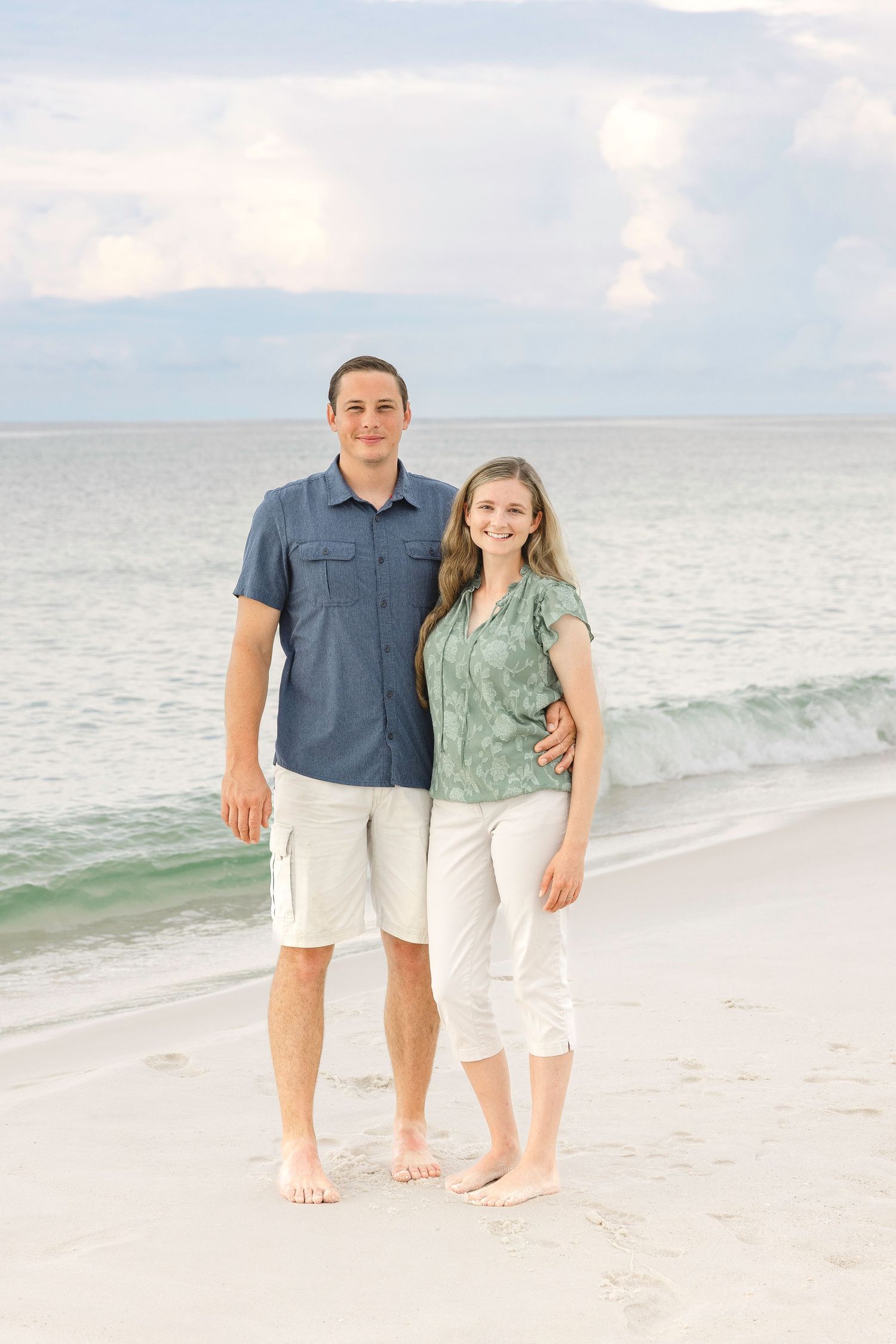 Two people standing together on a pristine white sand beach with calm ocean waters in the background.