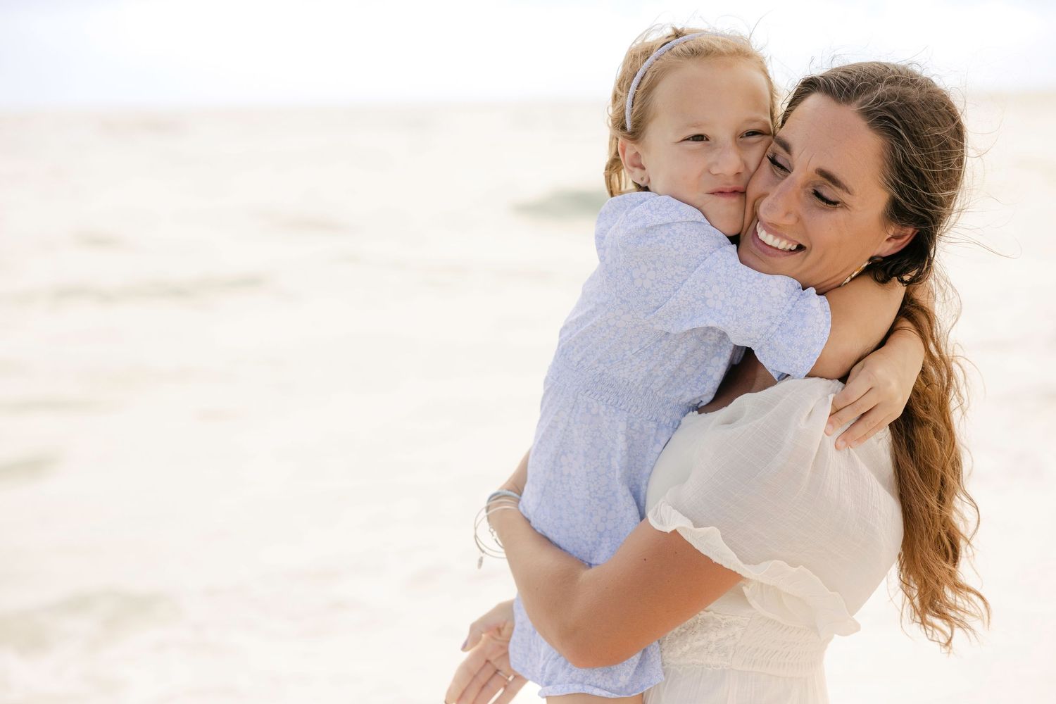 Parent and child share joyful embrace on sunny beach with white sand.