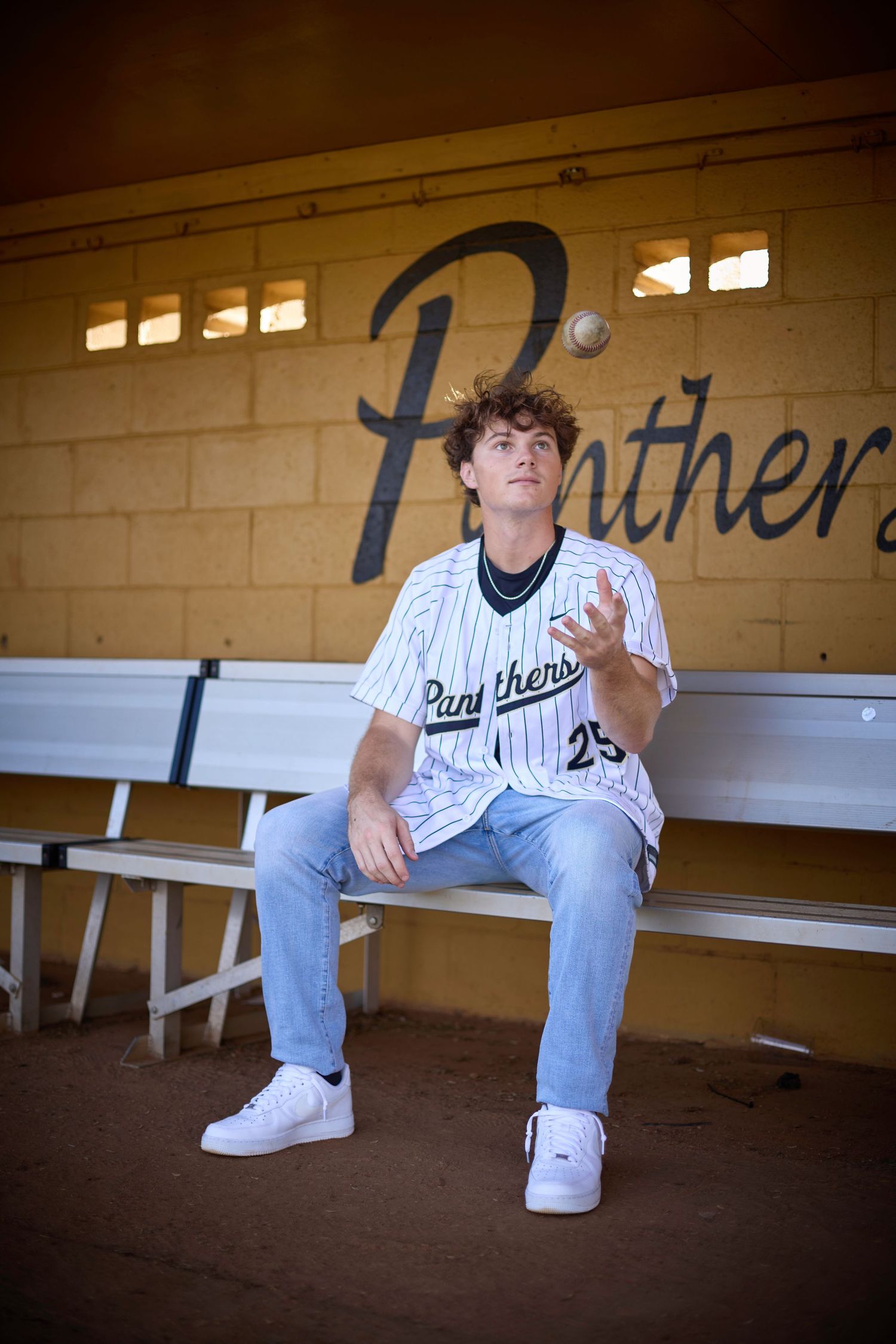 Baseball player lounging on dugout bench in Panthers uniform.