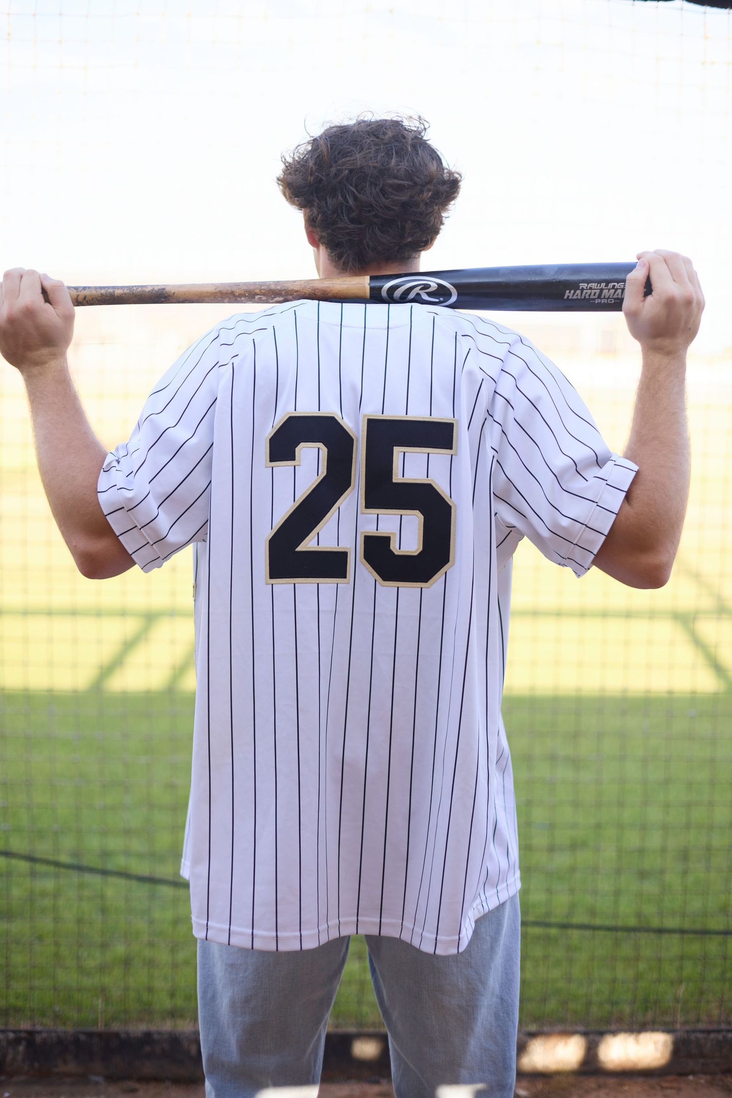 Baseball player in white pinstriped uniform number 25 shown from behind on field.