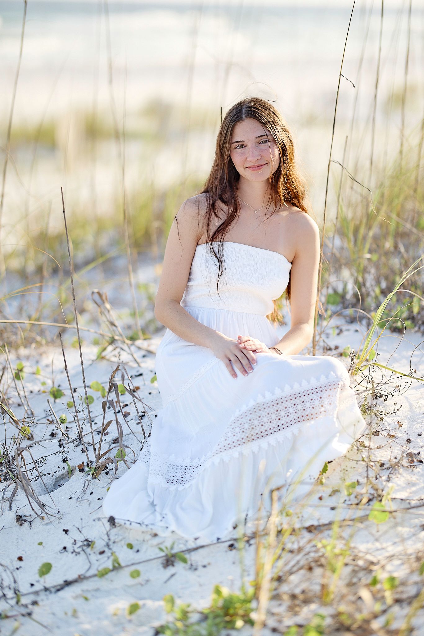 Summer photoshoot among beach dunes with white strapless dress and natural lighting.