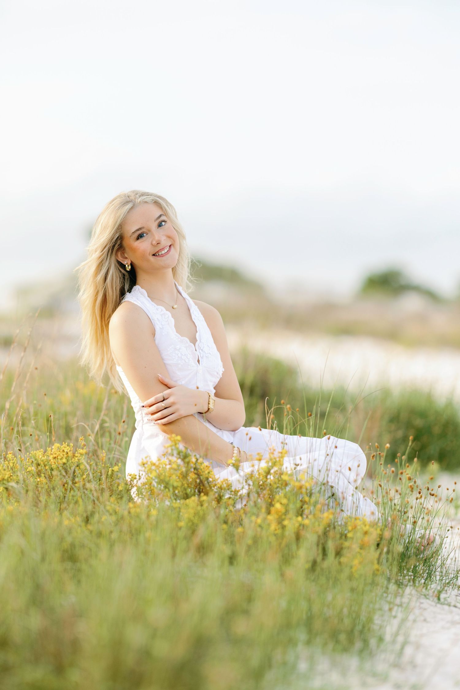 A person in a white dress sits in a sunny meadow filled with yellow wildflowers on a bright summer day.