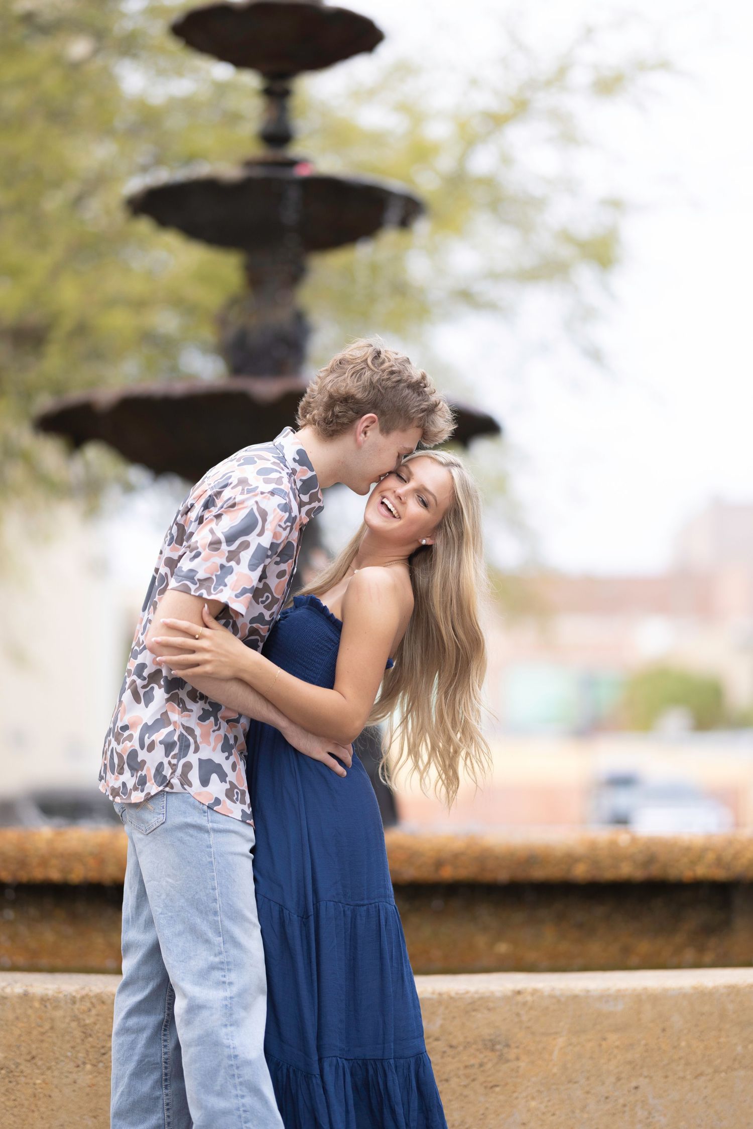 Joyful couple share laughs and embraces near a decorative fountain.