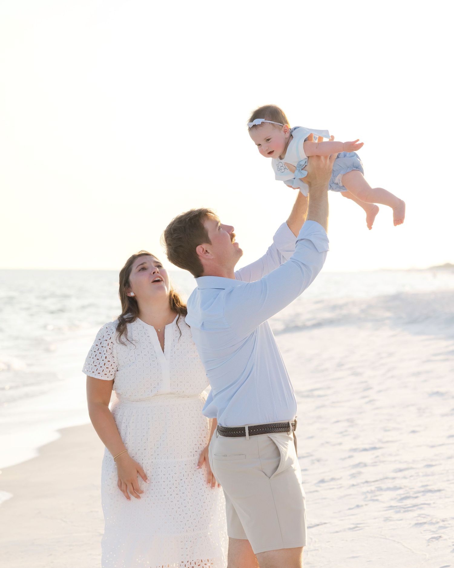 Family enjoying playful moments together on a sunny beach with white sand.