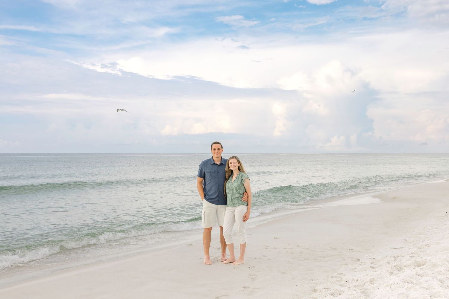 A scenic beach landscape with white sand and gentle waves under a bright blue sky.