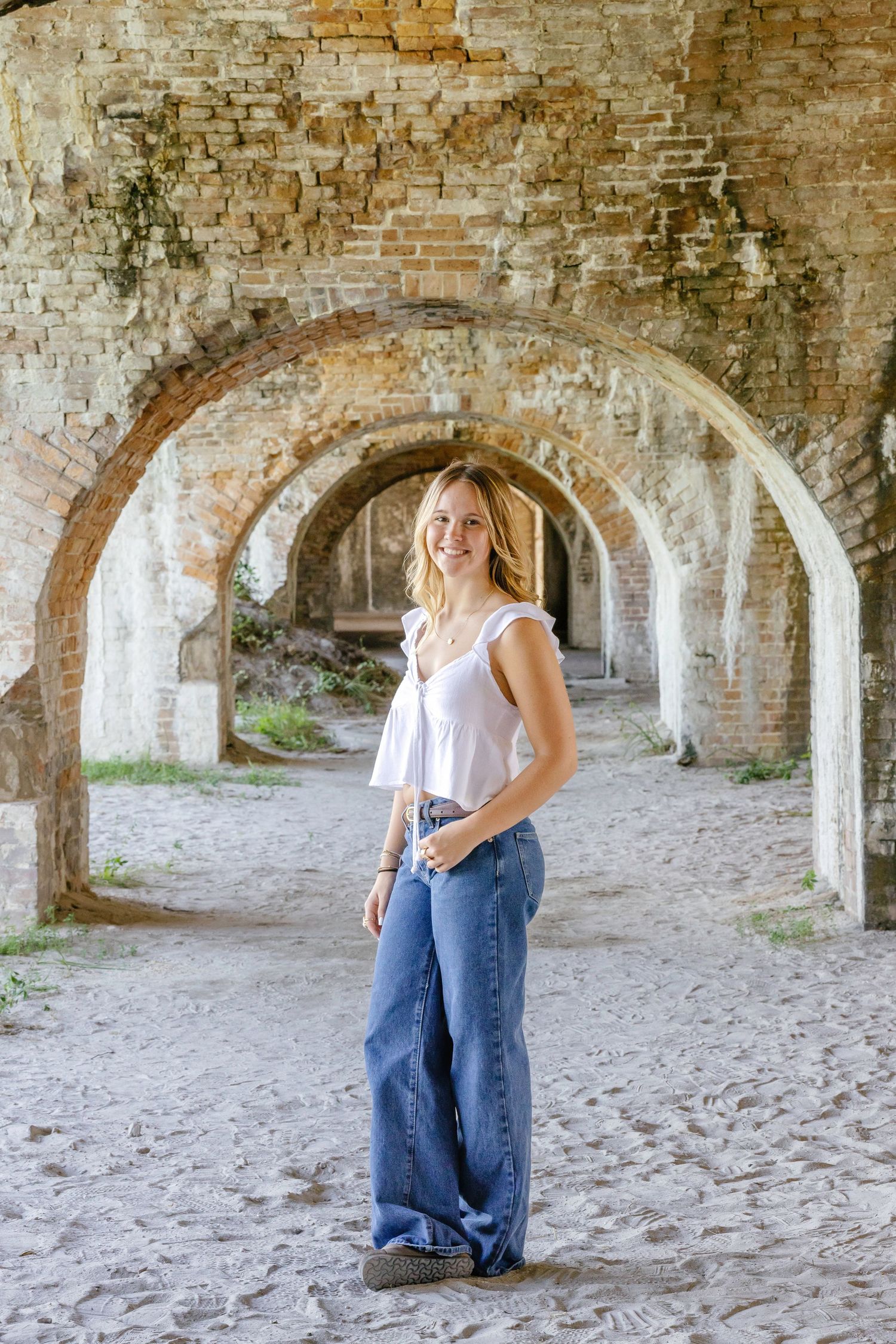 A person wearing jeans and a white top stands beneath historic stone arches at Fort Morgan, Alabama.