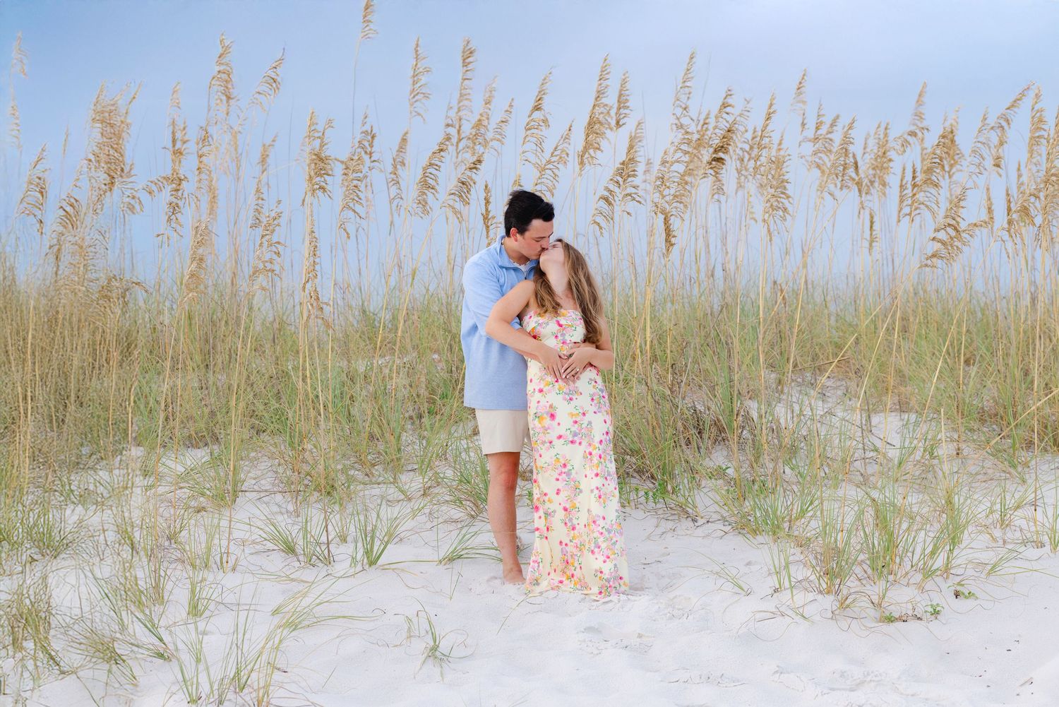 A couple poses together among tall beach grass and dunes during a seaside photoshoot.