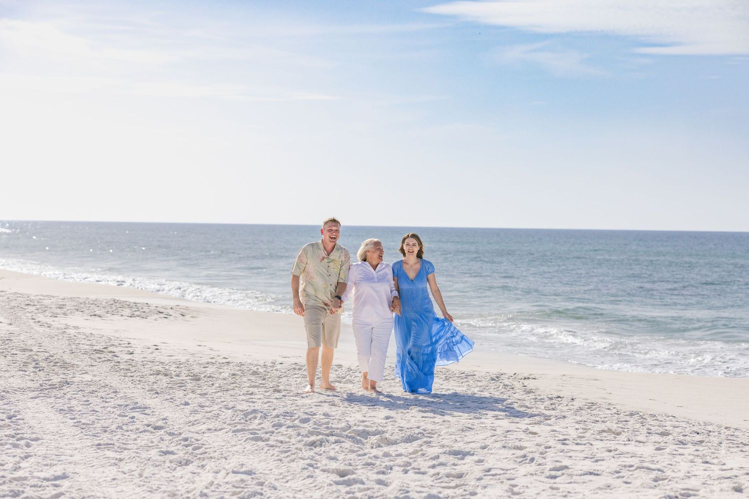 Three people walking on a sunny white sand beach with calm ocean waves in the background.