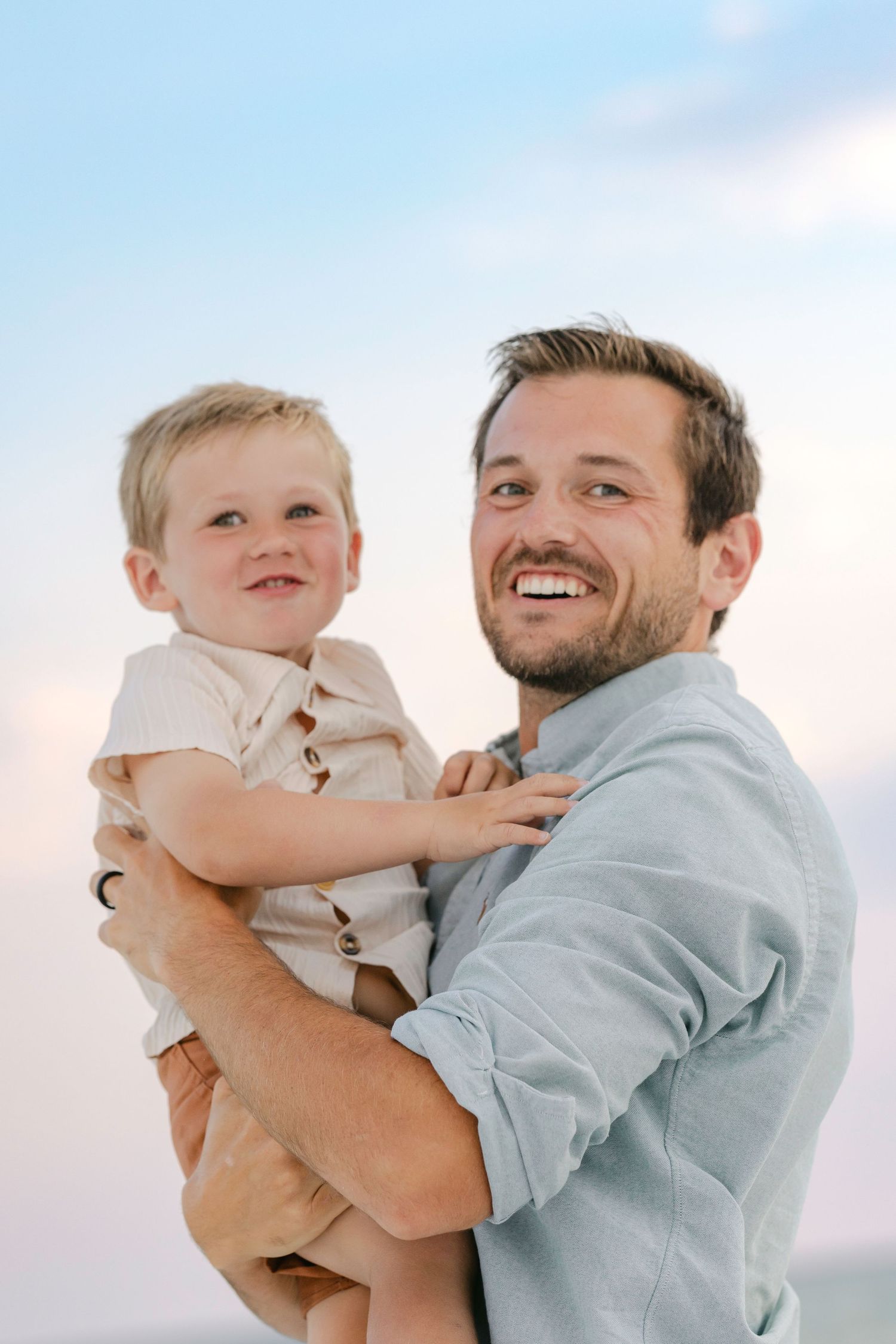 A parent and child play together outdoors in a series of joyful, candid moments against a bright sky.