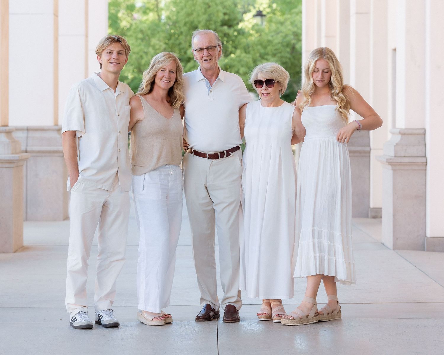 Family of five posing together in white and neutral outfits for a portrait outdoors.