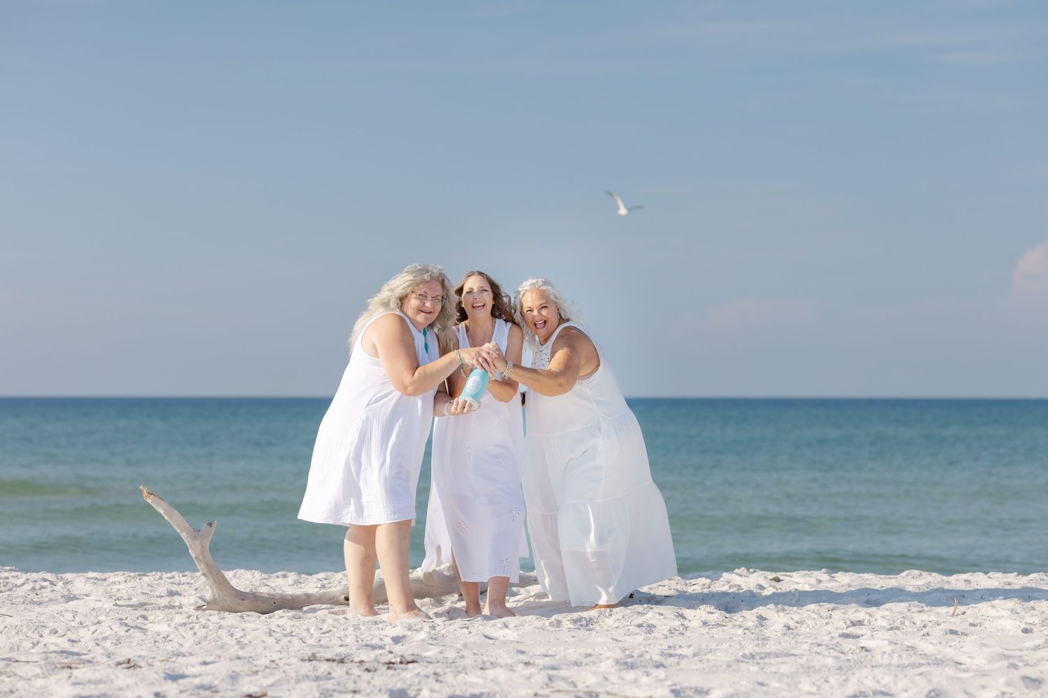 Family group in white outfits having their photos taken along a serene beach with blue ocean waters.