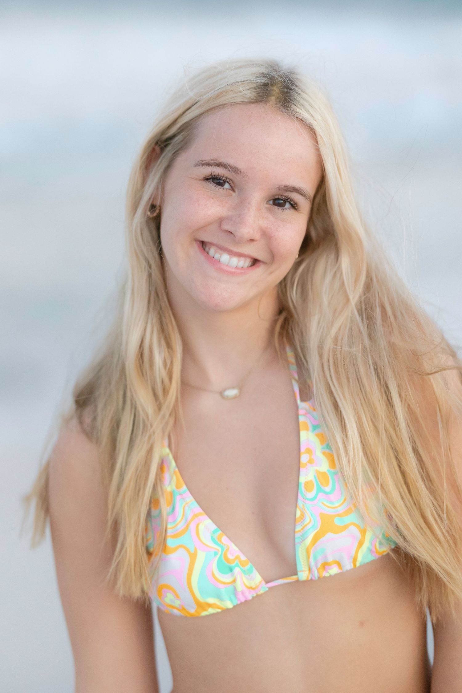 Portrait of person in colorful bikini top on beach with ocean backdrop.