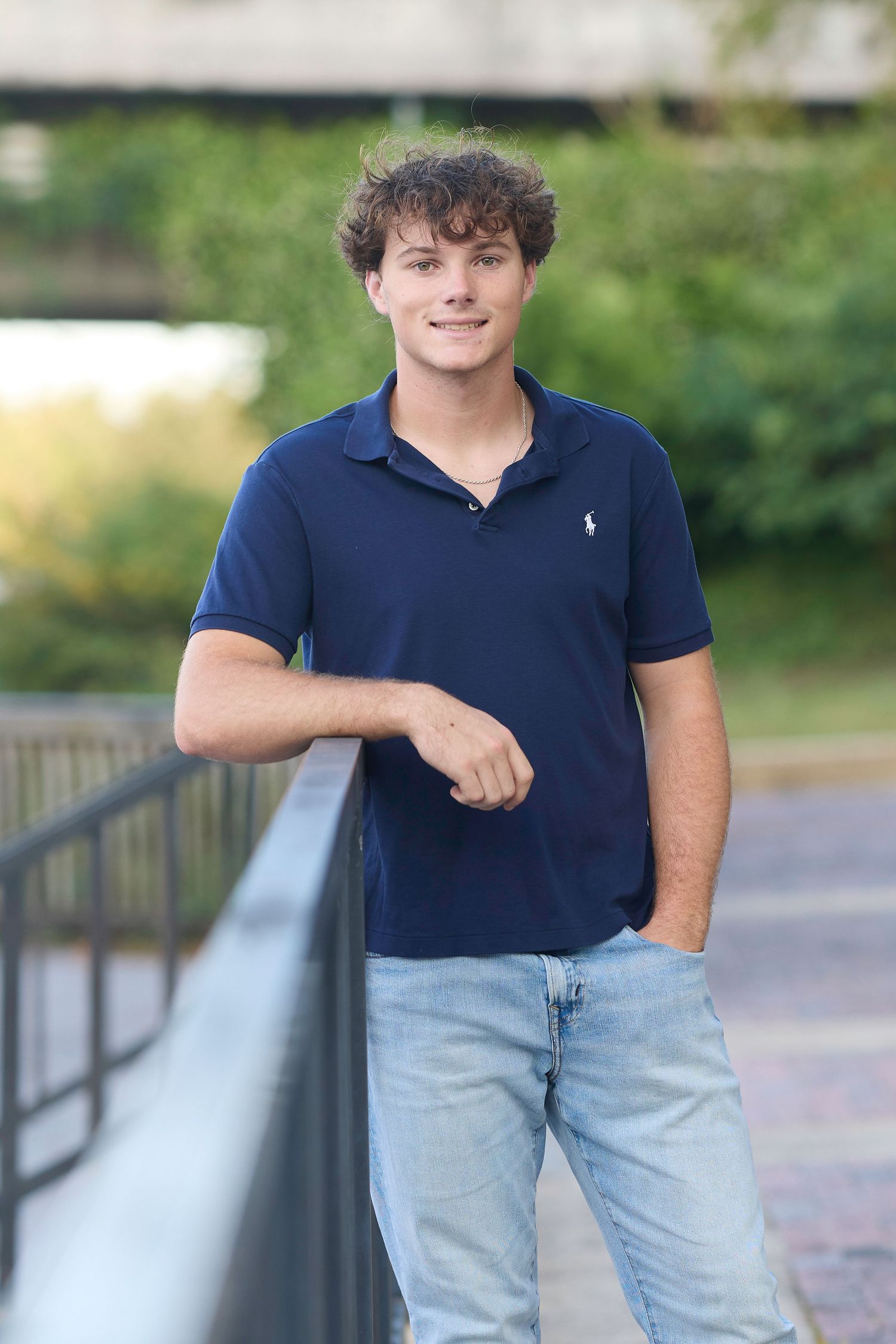 Outdoor portrait of athlete in navy polo shirt standing by railing.