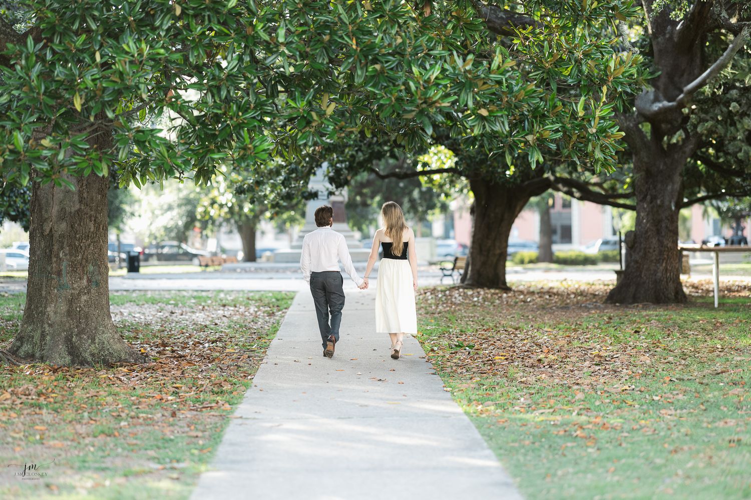 Couple walking down tree-lined pathway holding hands.